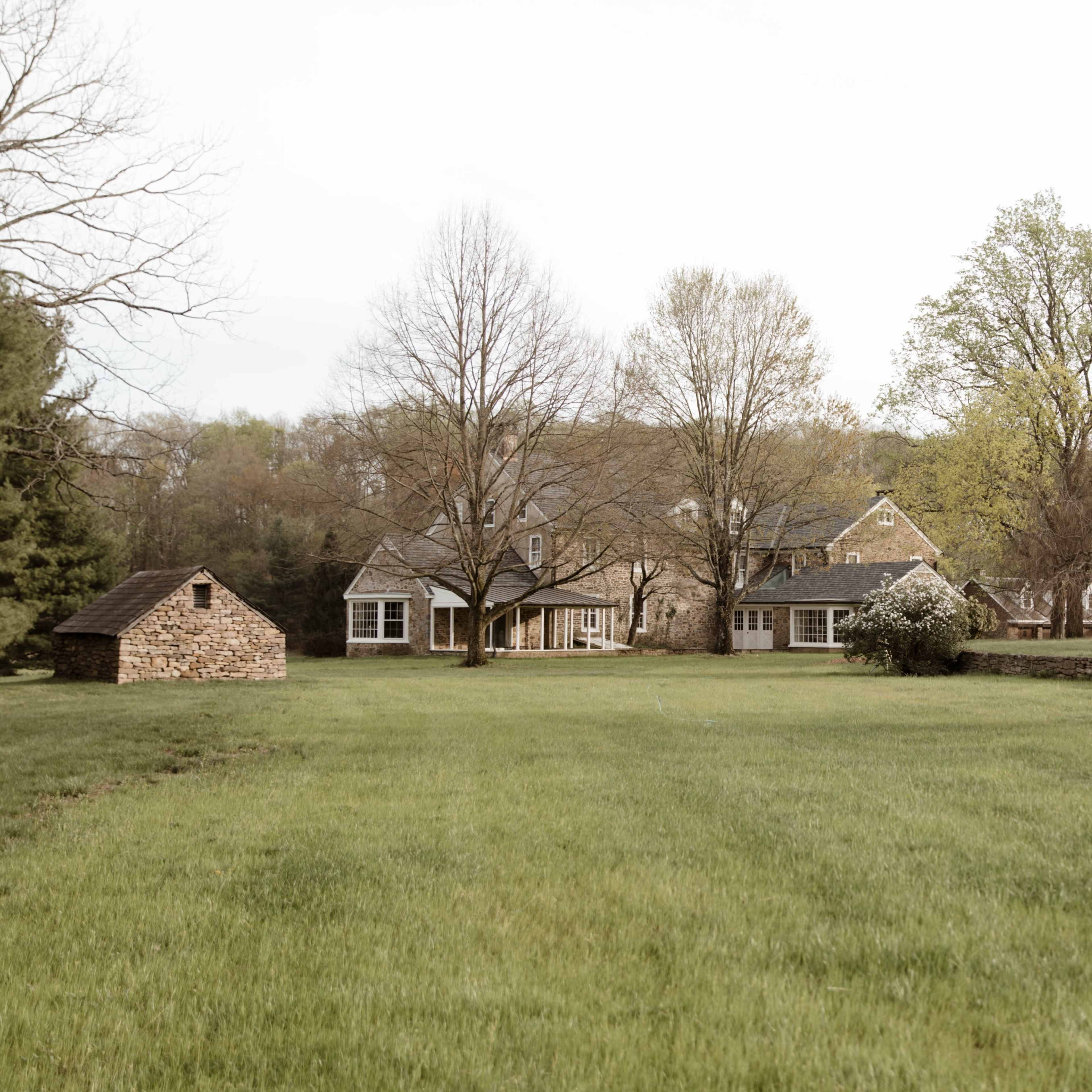 A large grassy area features a house with multiple windows, surrounded by trees and a blooming pink tree.