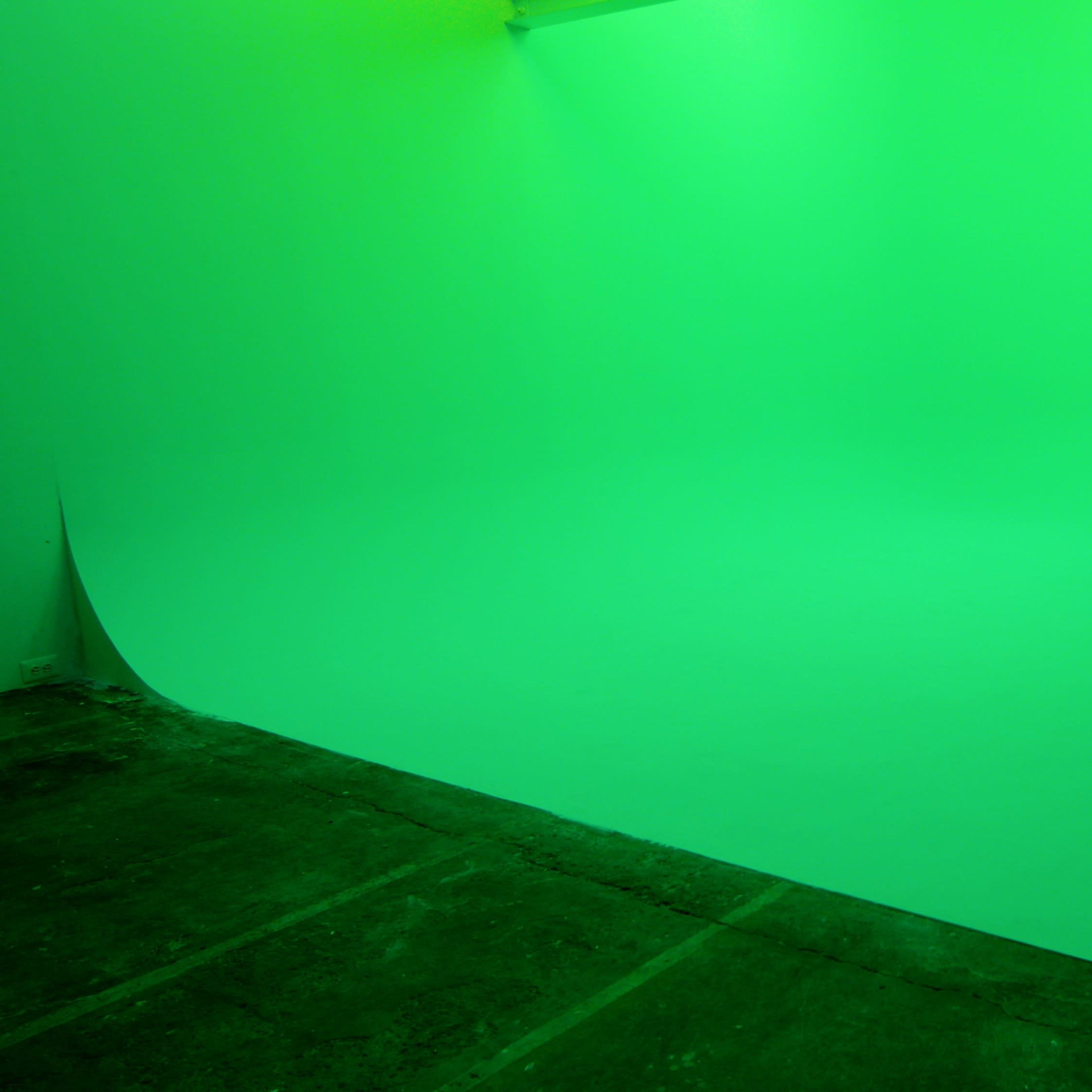 A room with green walls and a green floor, illuminated by artificial light.