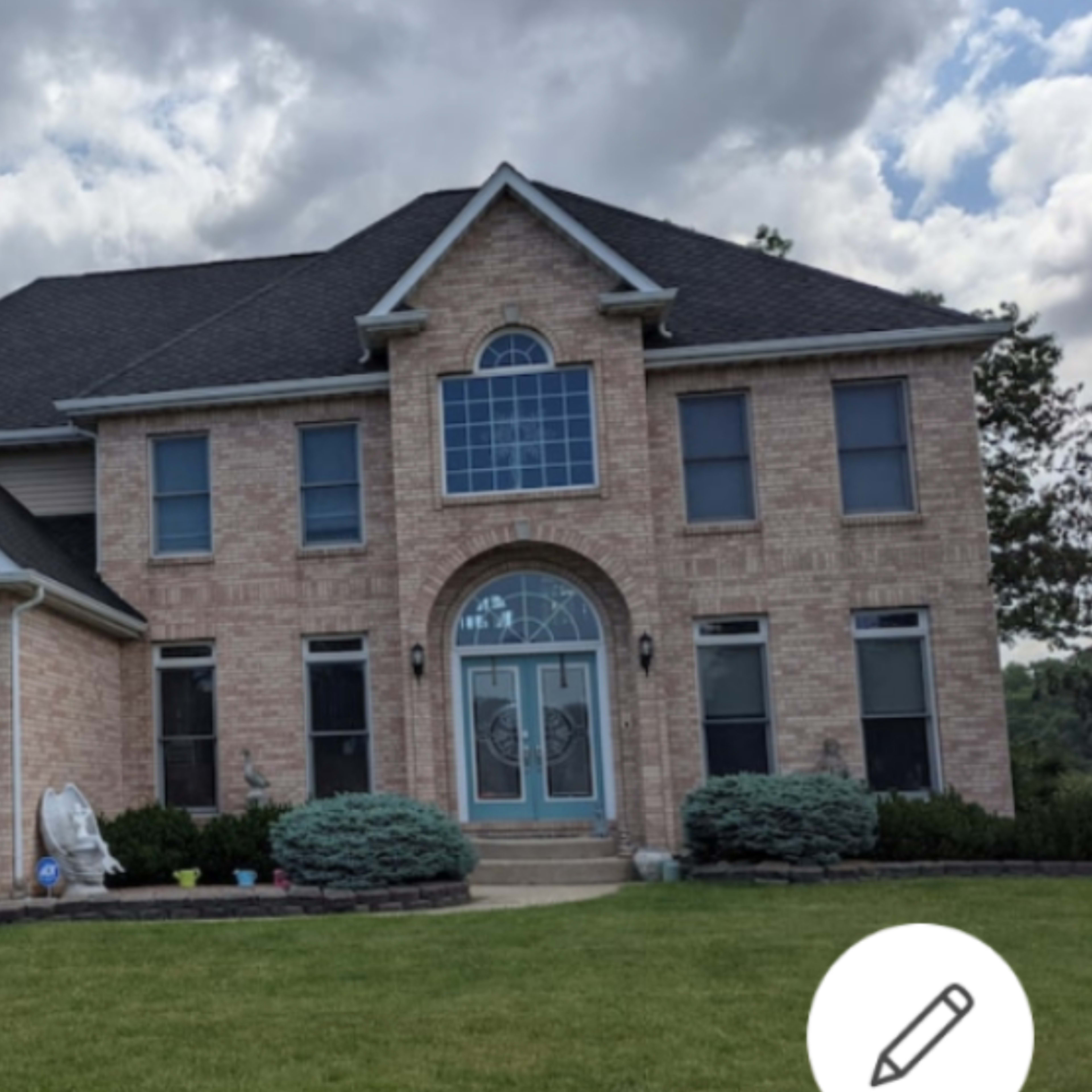 A large brick house with multiple windows and a prominent front entrance, surrounded by a well-maintained lawn and landscaping.