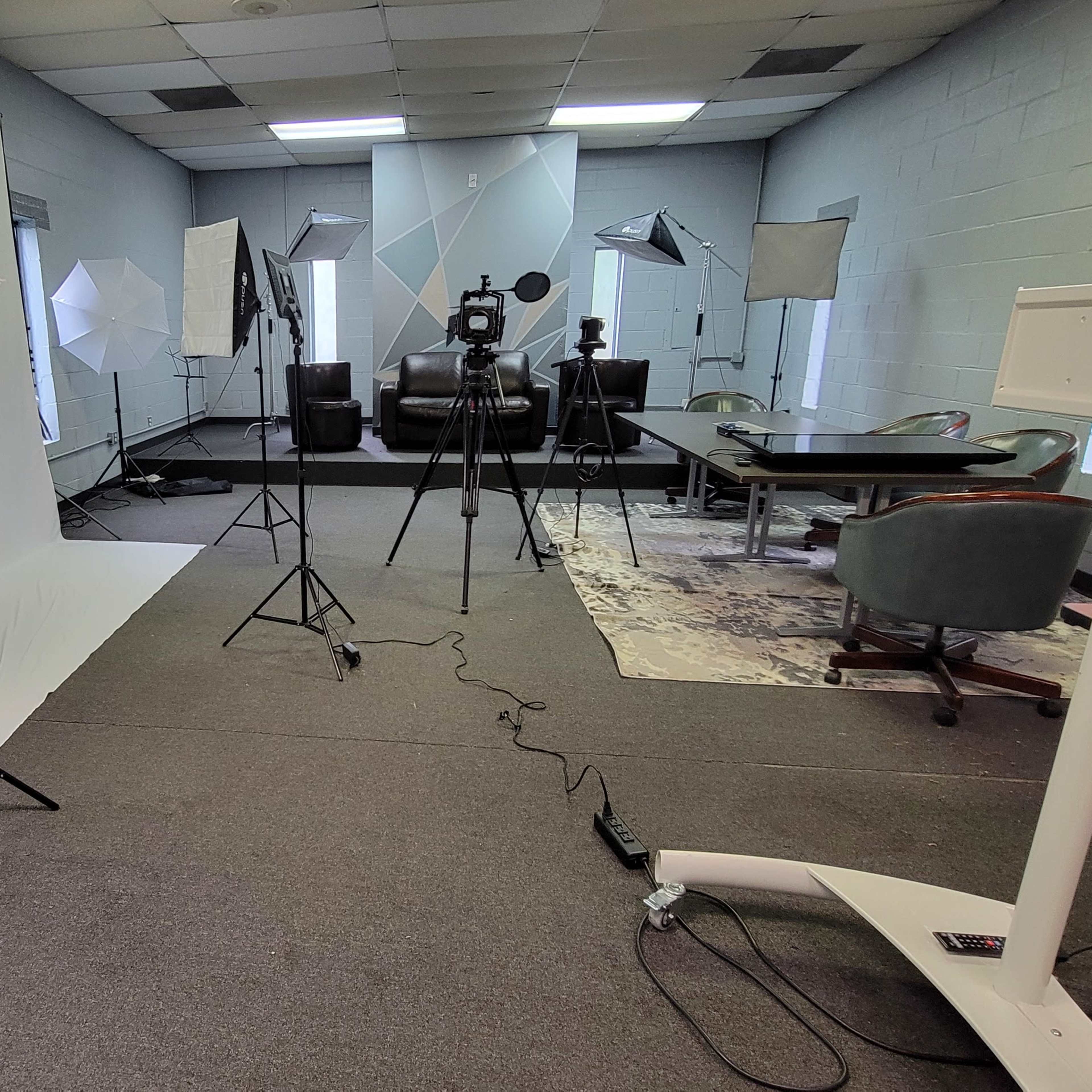 A photography studio setup with multiple lights, tripods, and a large table in a room with gray walls and carpet.