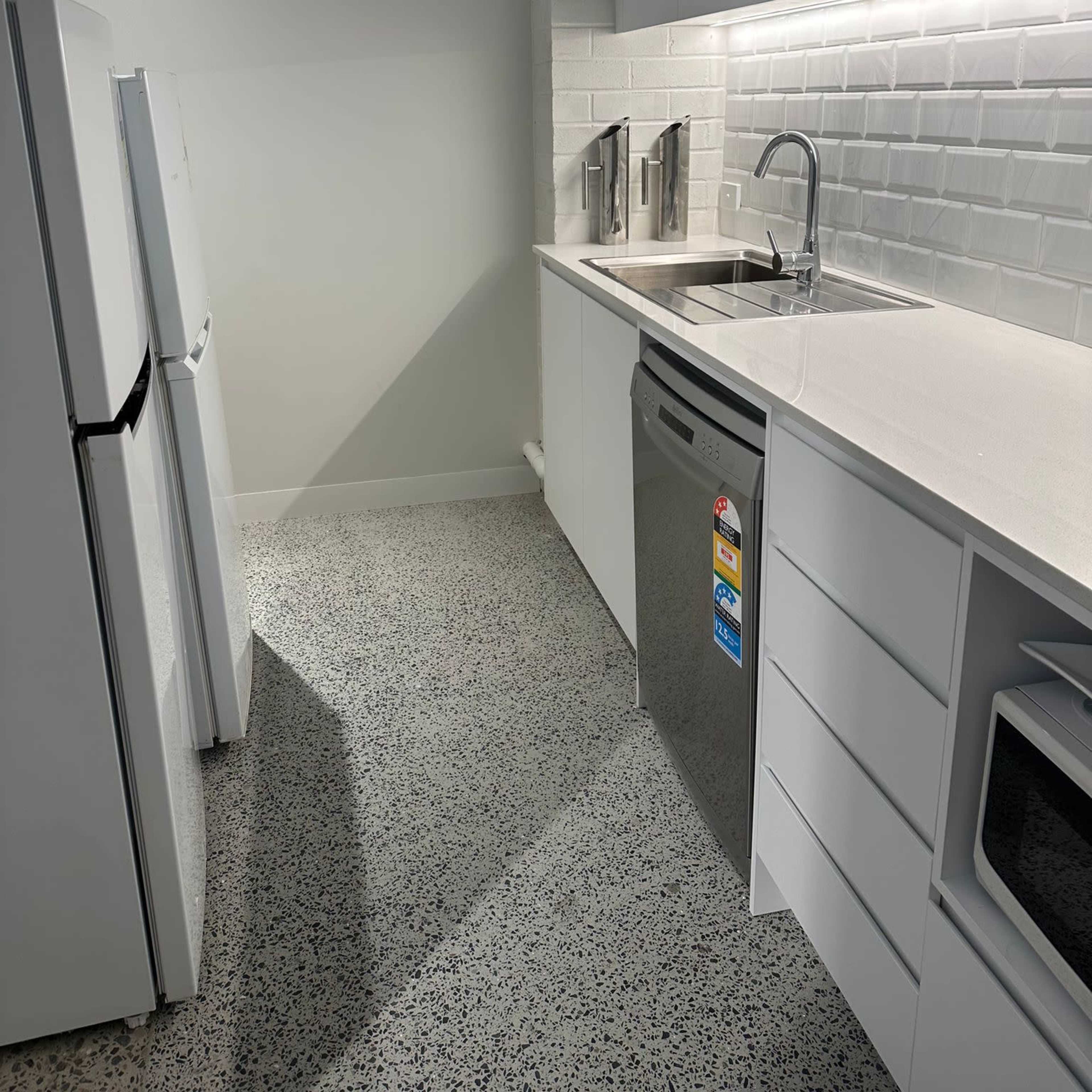 A modern kitchen featuring a white refrigerator, a sink with a faucet, and a dishwasher, along with white cabinetry and a light-colored countertop.
