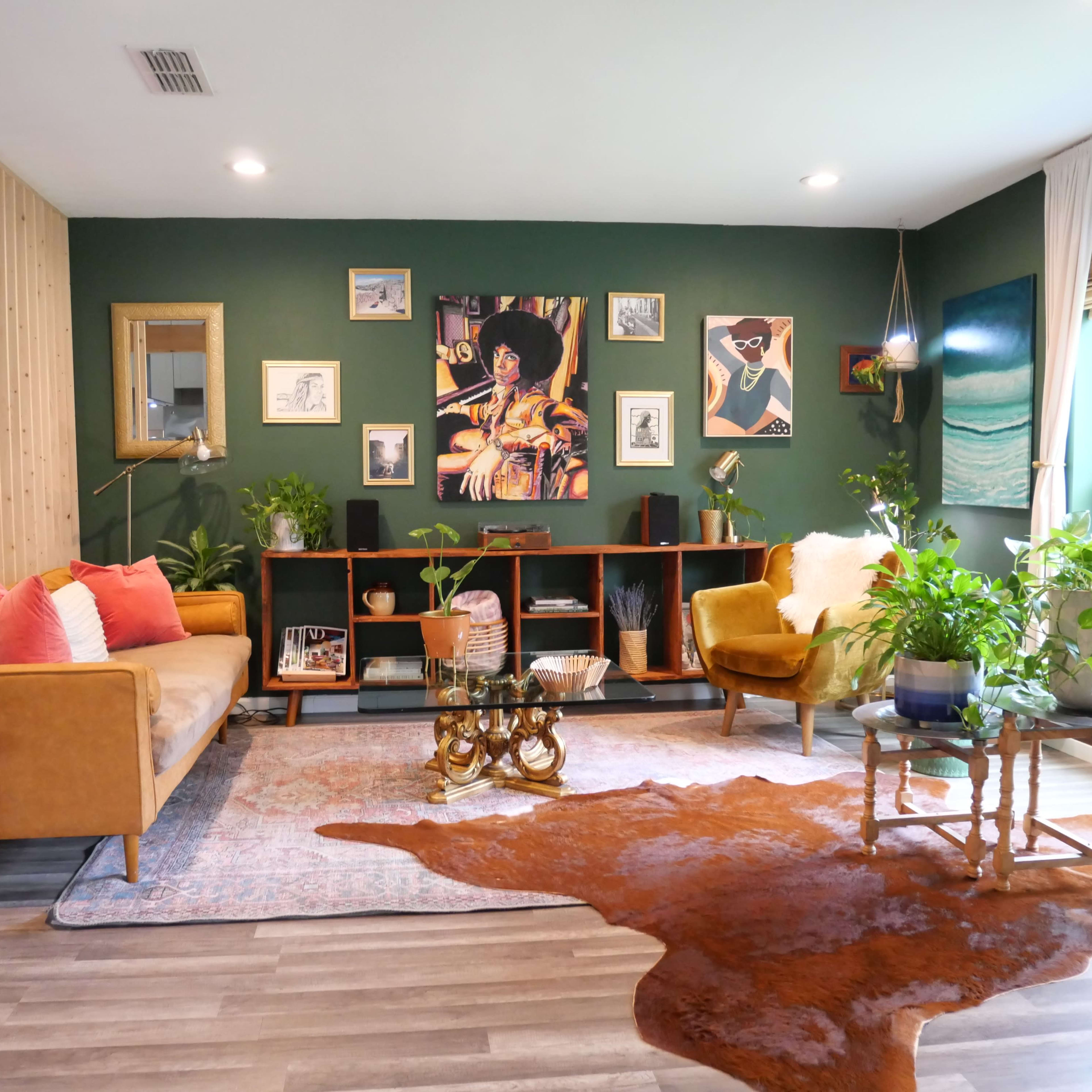 A stylish living room with a green accent wall, a brown sofa, a yellow armchair, a wooden shelf with art and plants, and a rug on the floor.