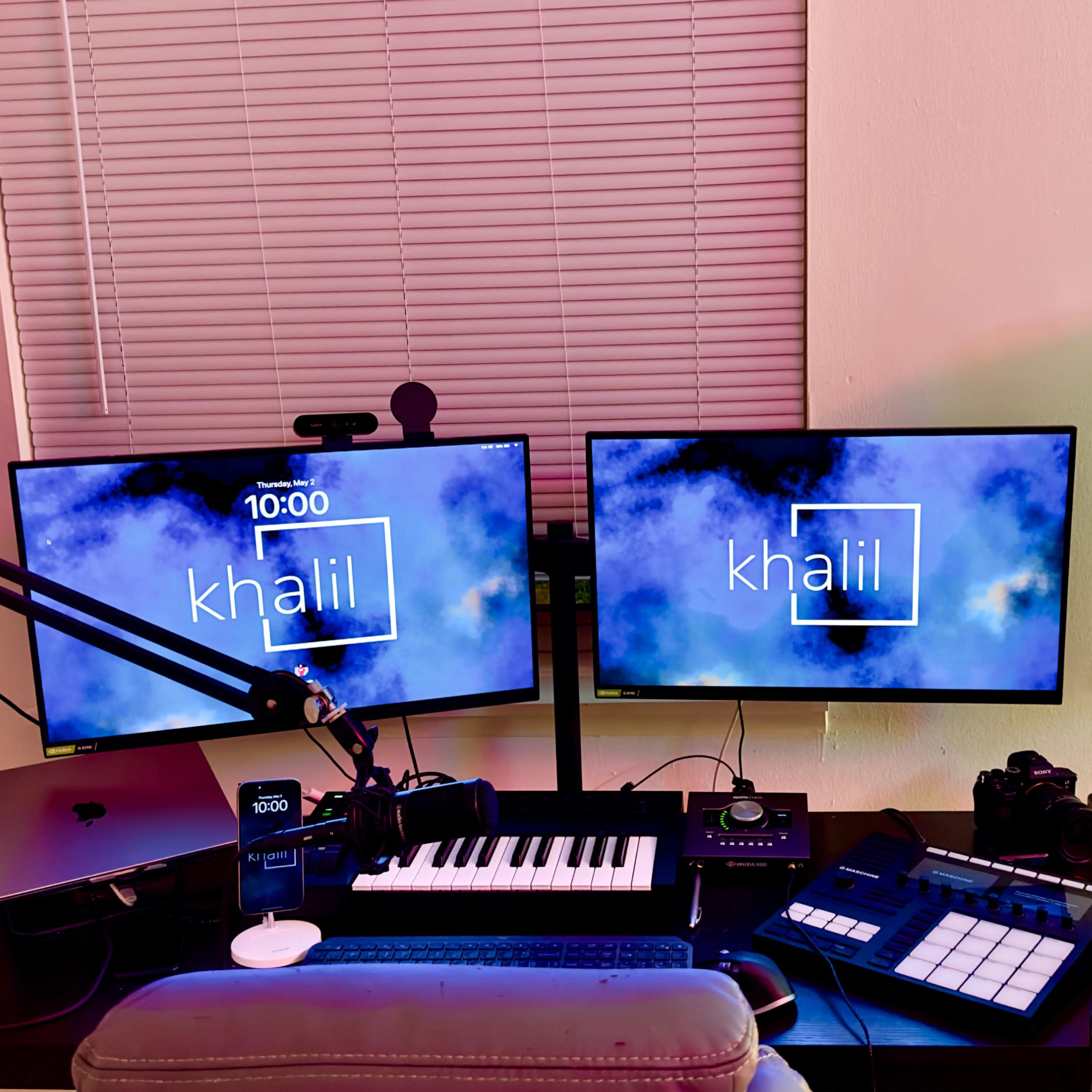 A workspace with two monitors displaying the name "khalil," a keyboard, audio equipment, and a camera, all arranged on a desk.