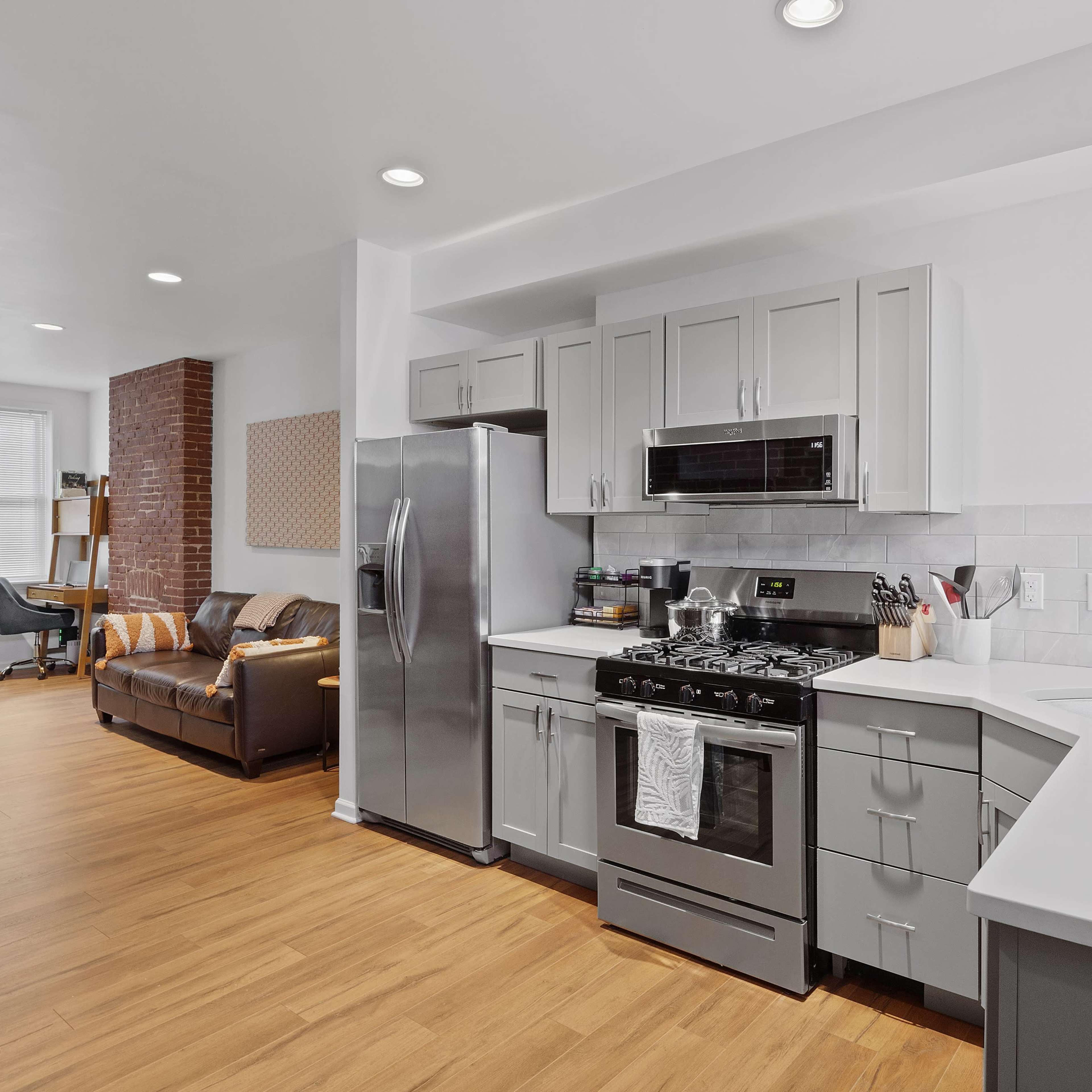 A modern kitchen features stainless steel appliances, gray cabinetry, and an open layout that connects to a living area with a brown couch.