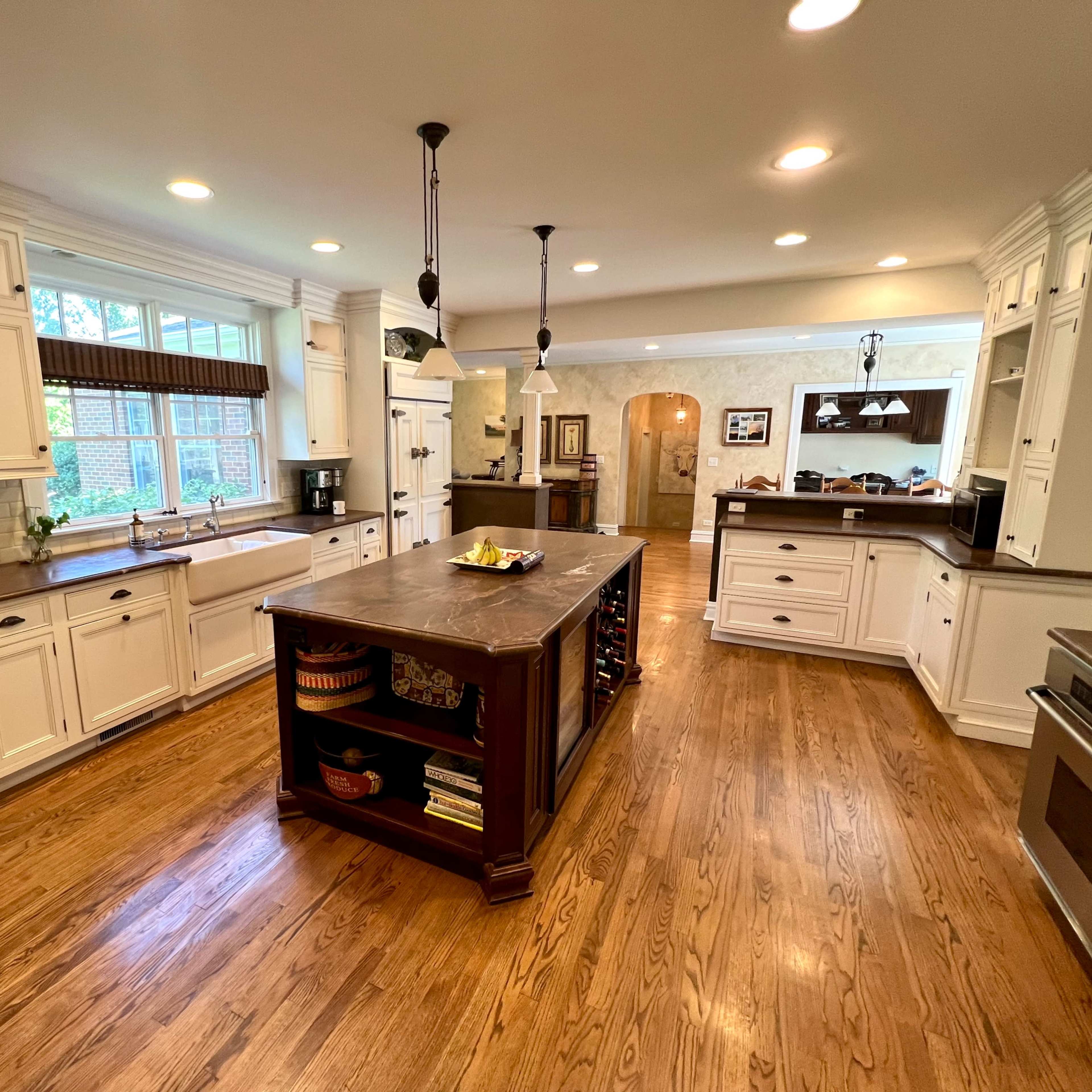 A spacious kitchen features white cabinetry, a central island with a dark countertop, and hardwood floors.