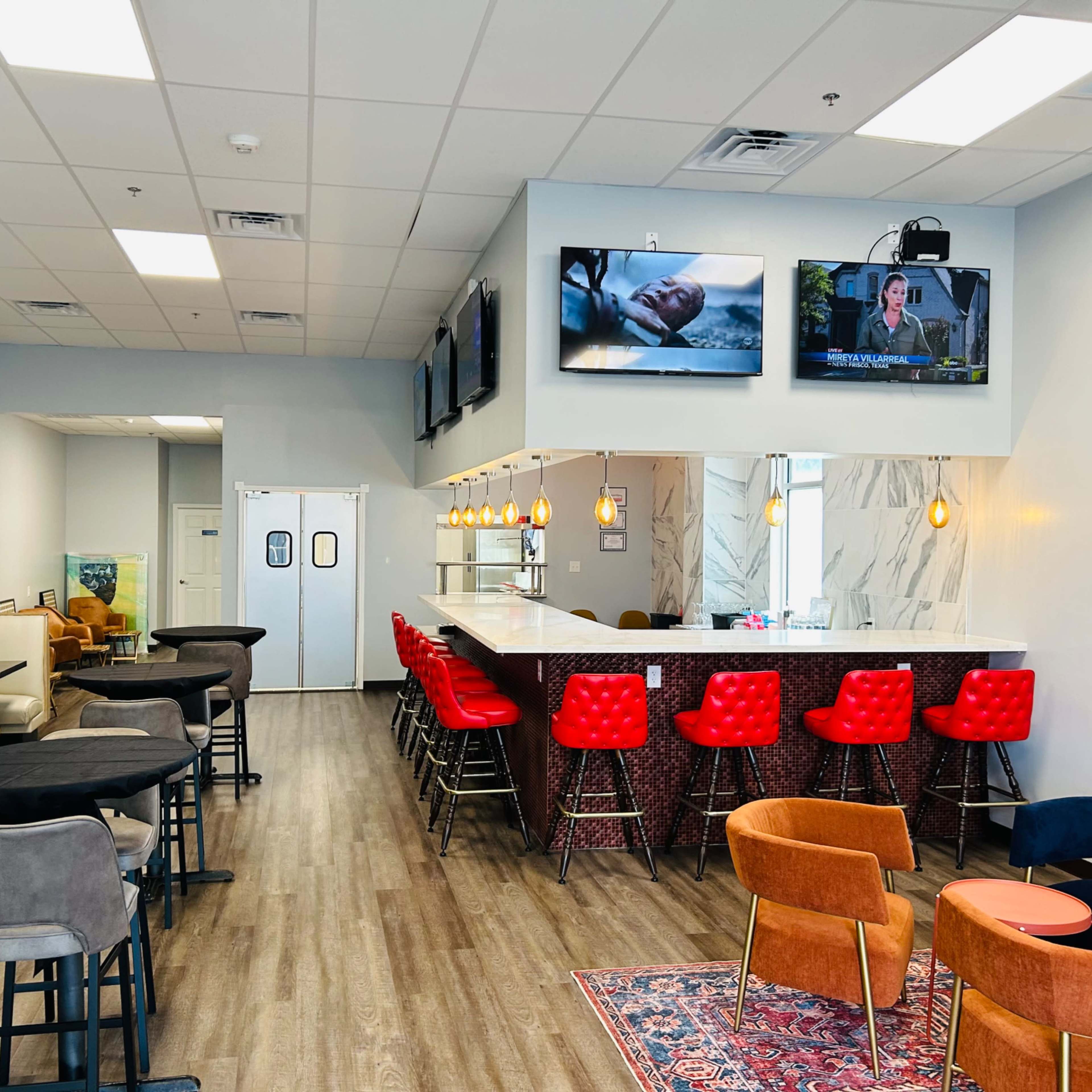 A modern cafe interior with booths, a bar area with red stools, and multiple televisions mounted on the walls.