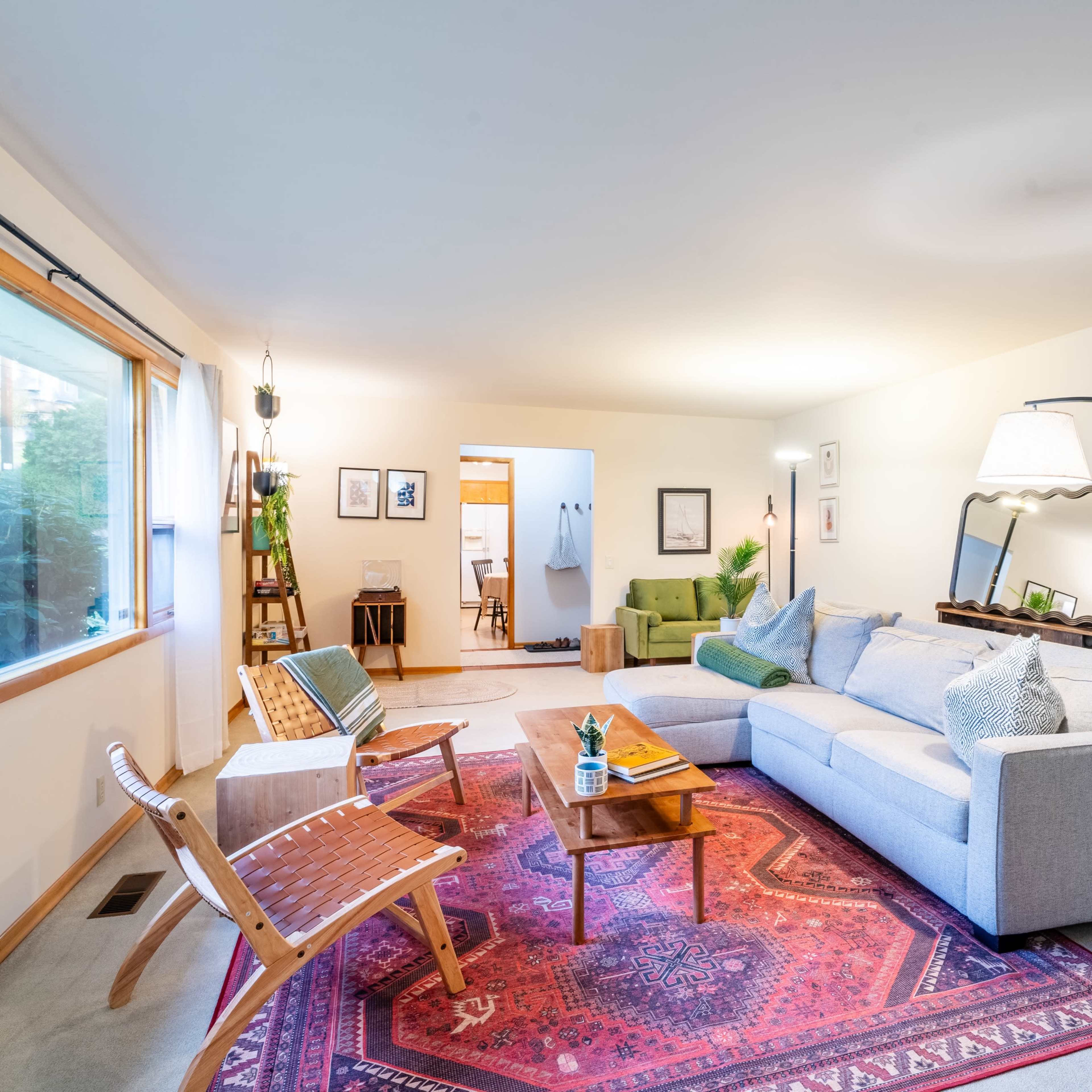 A cozy living room with a gray sofa, a wooden coffee table on a patterned rug, and large windows providing natural light.