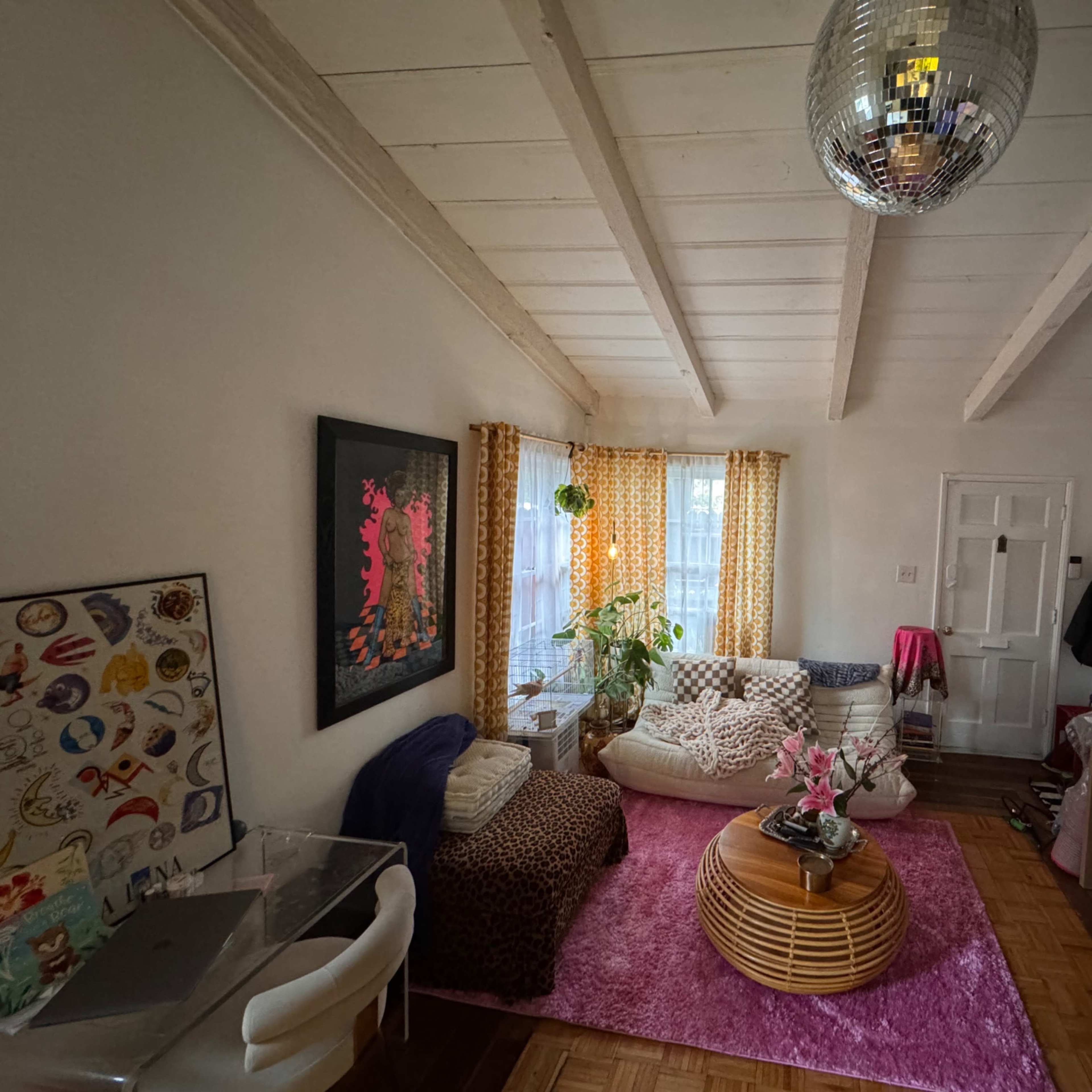 A cozy living room with a circular coffee table, a white sofa, patterned curtains, and a disco ball hanging from the ceiling.