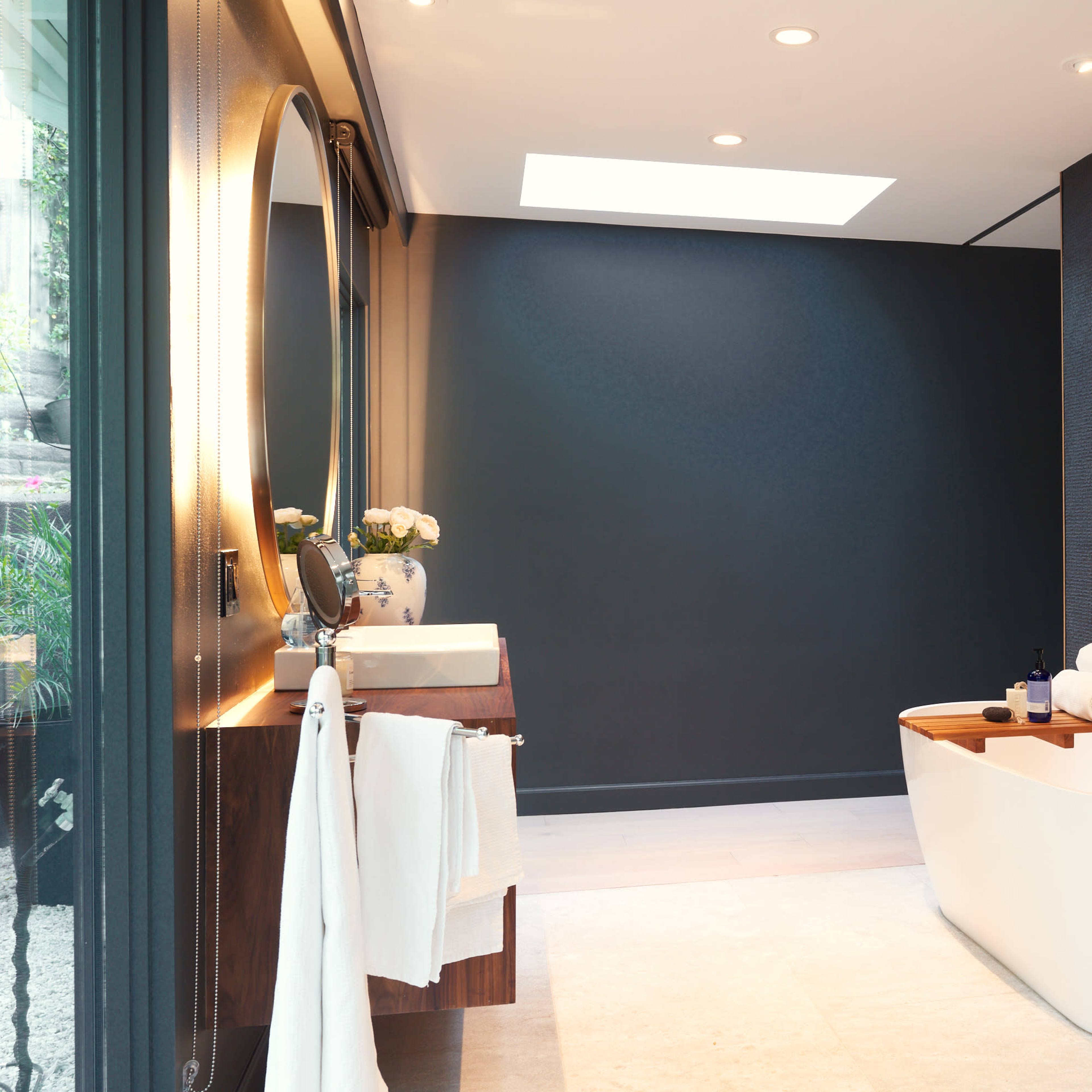 A modern bathroom featuring a freestanding tub, a round mirror above a sink, and a wall with a textured finish.