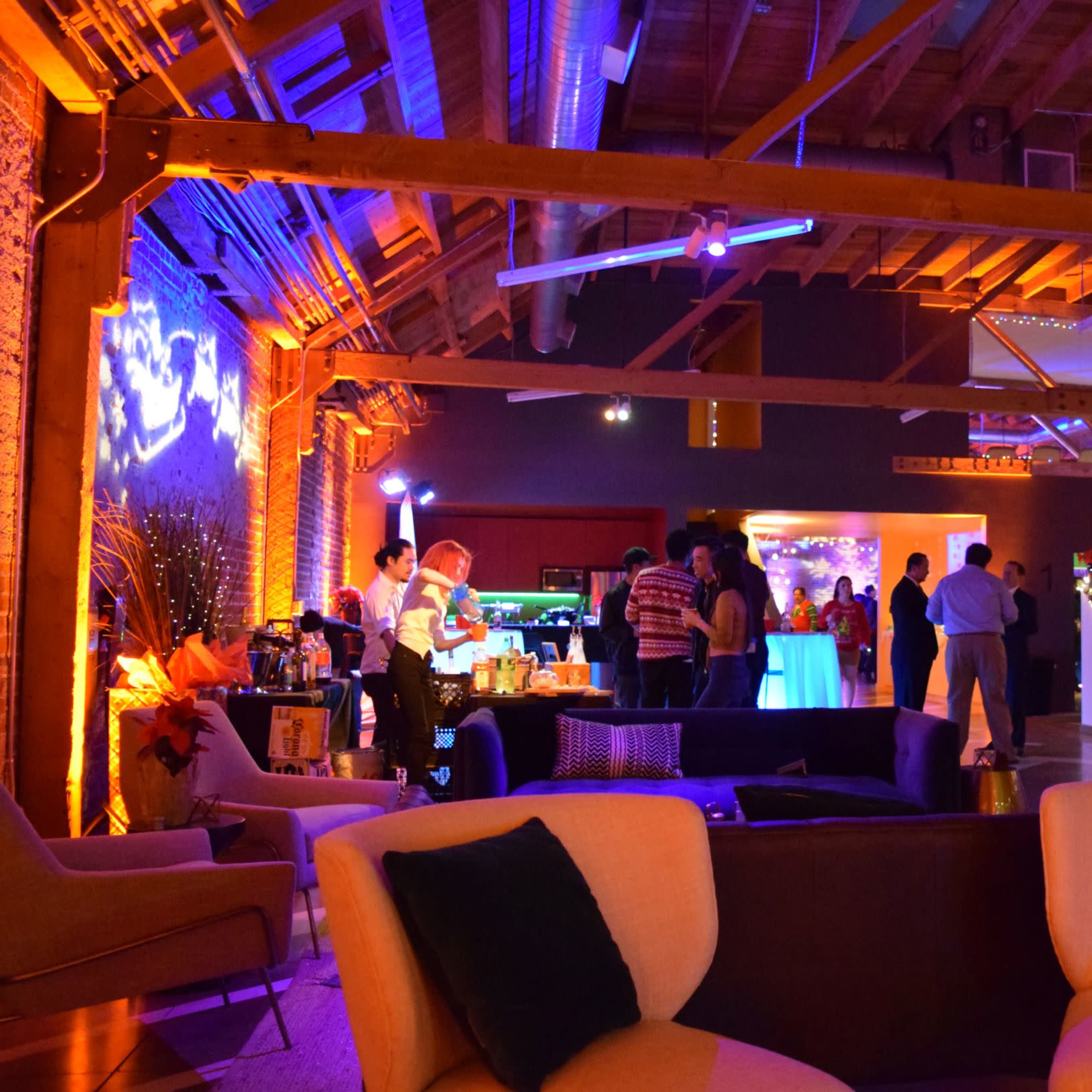 A vibrant event space features guests socializing under colorful lighting, with a bar area to the left and festive decorations throughout.