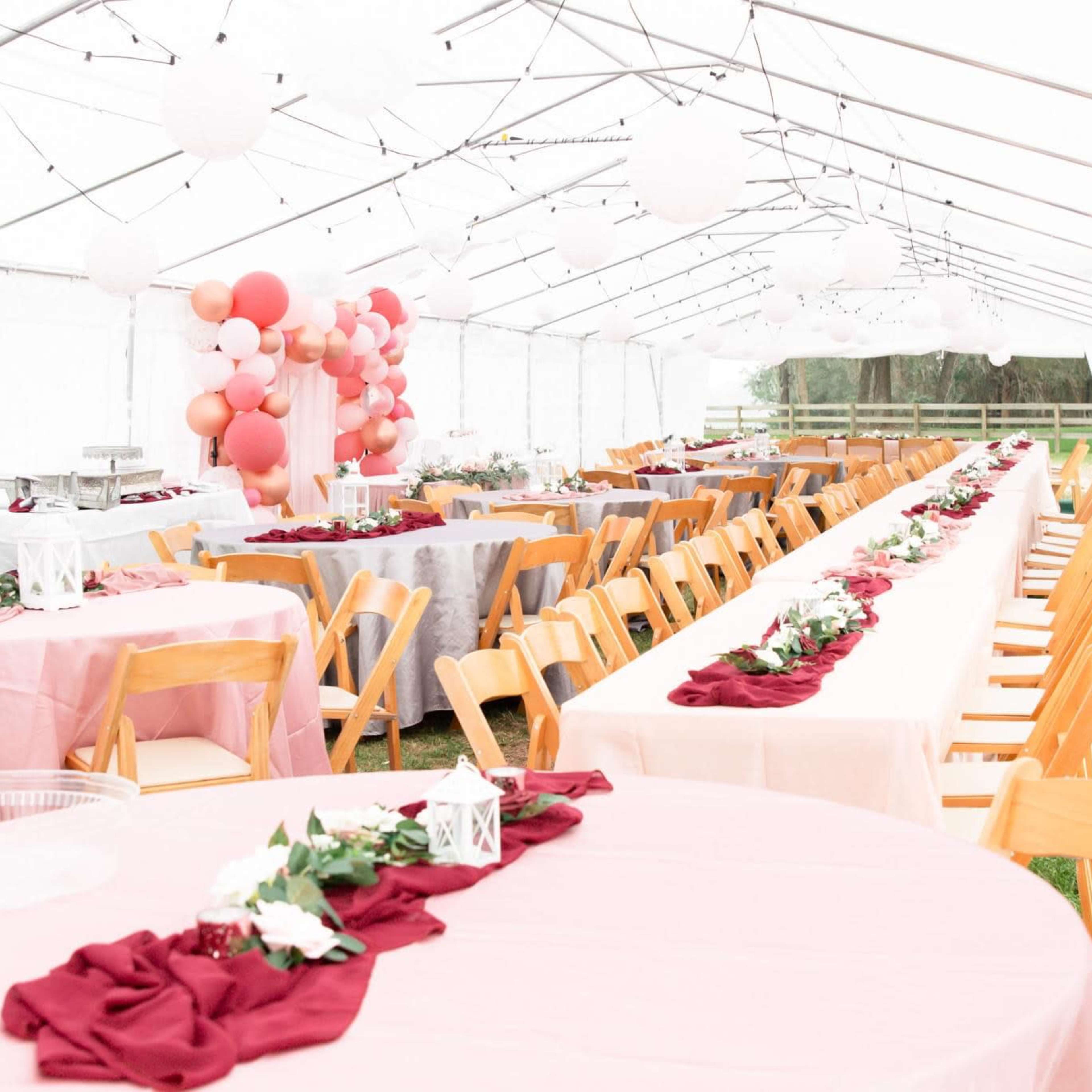 A large outdoor tent is set up for a banquet with rows of tables covered in various colored linens and decorated with floral centerpieces.