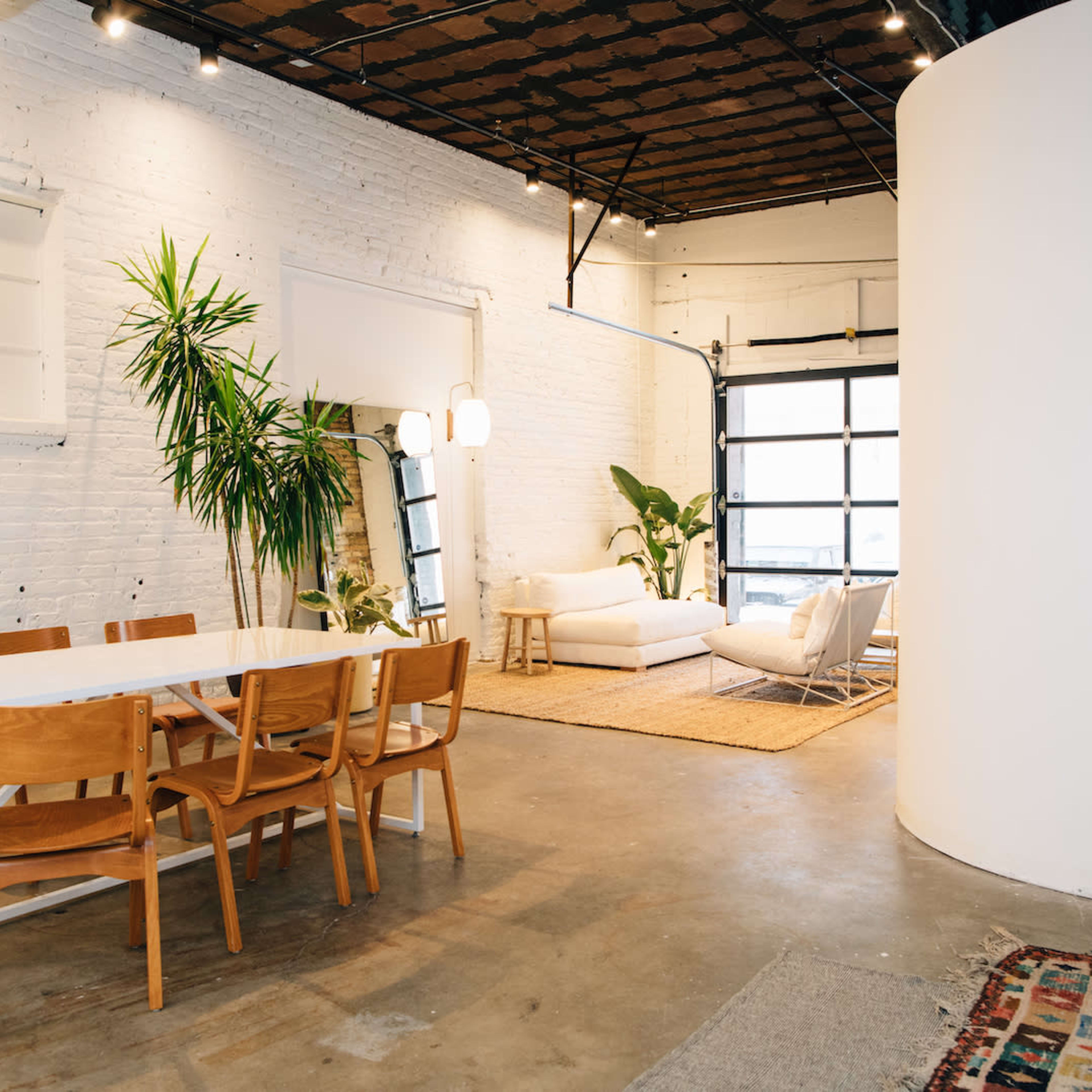 A spacious, modern interior featuring a dining area with a table and chairs, a living space with a sofa, and a large window.
