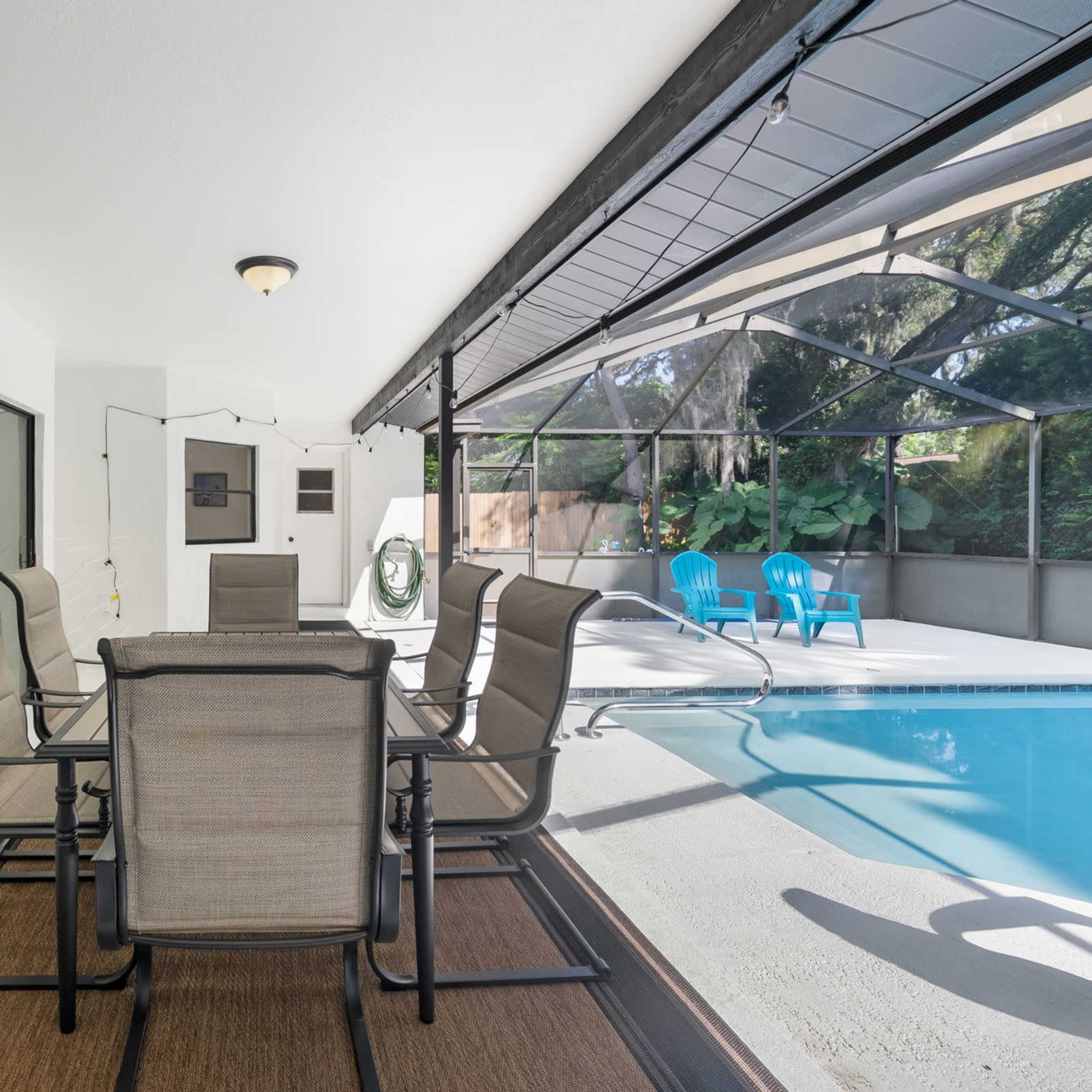 A covered patio area with a dining table and chairs overlooking a pool enclosed by a screen.