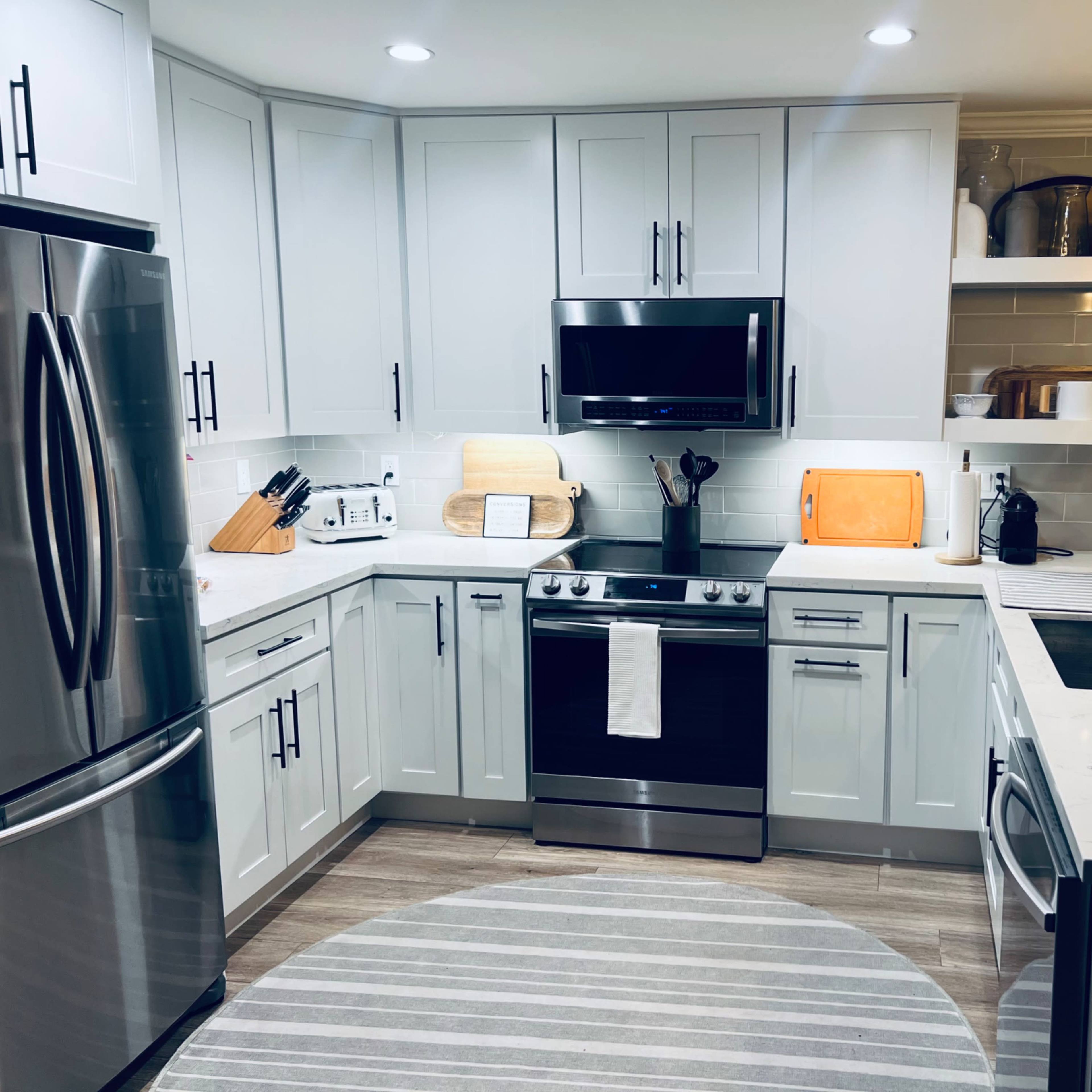 A modern kitchen with light gray cabinets, stainless steel appliances, and a circular rug on the floor.