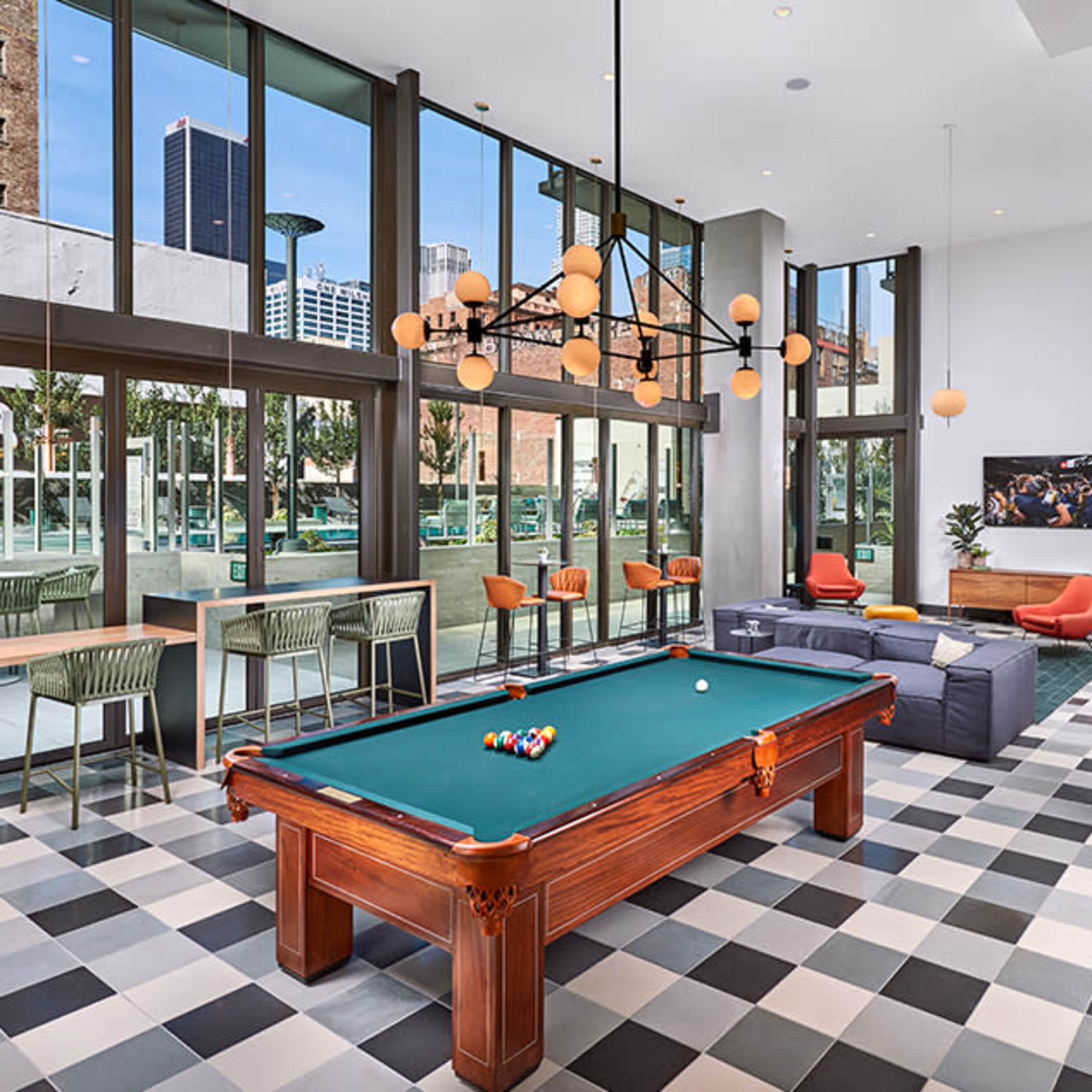 A modern recreational room featuring a pool table, seating areas, and large windows with urban views.