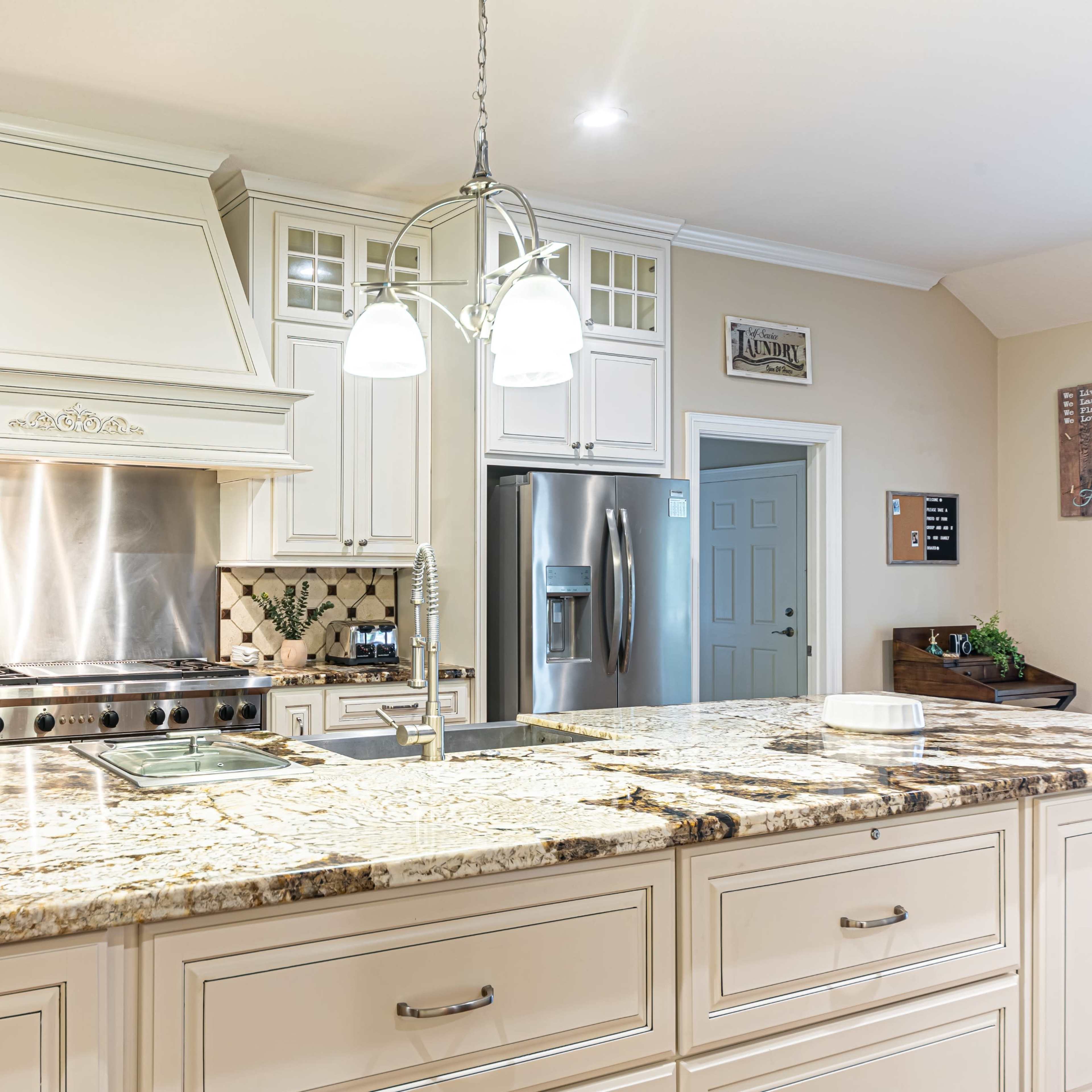 A spacious kitchen features a large marble island, stainless steel appliances, and a gas range with a decorative hood.