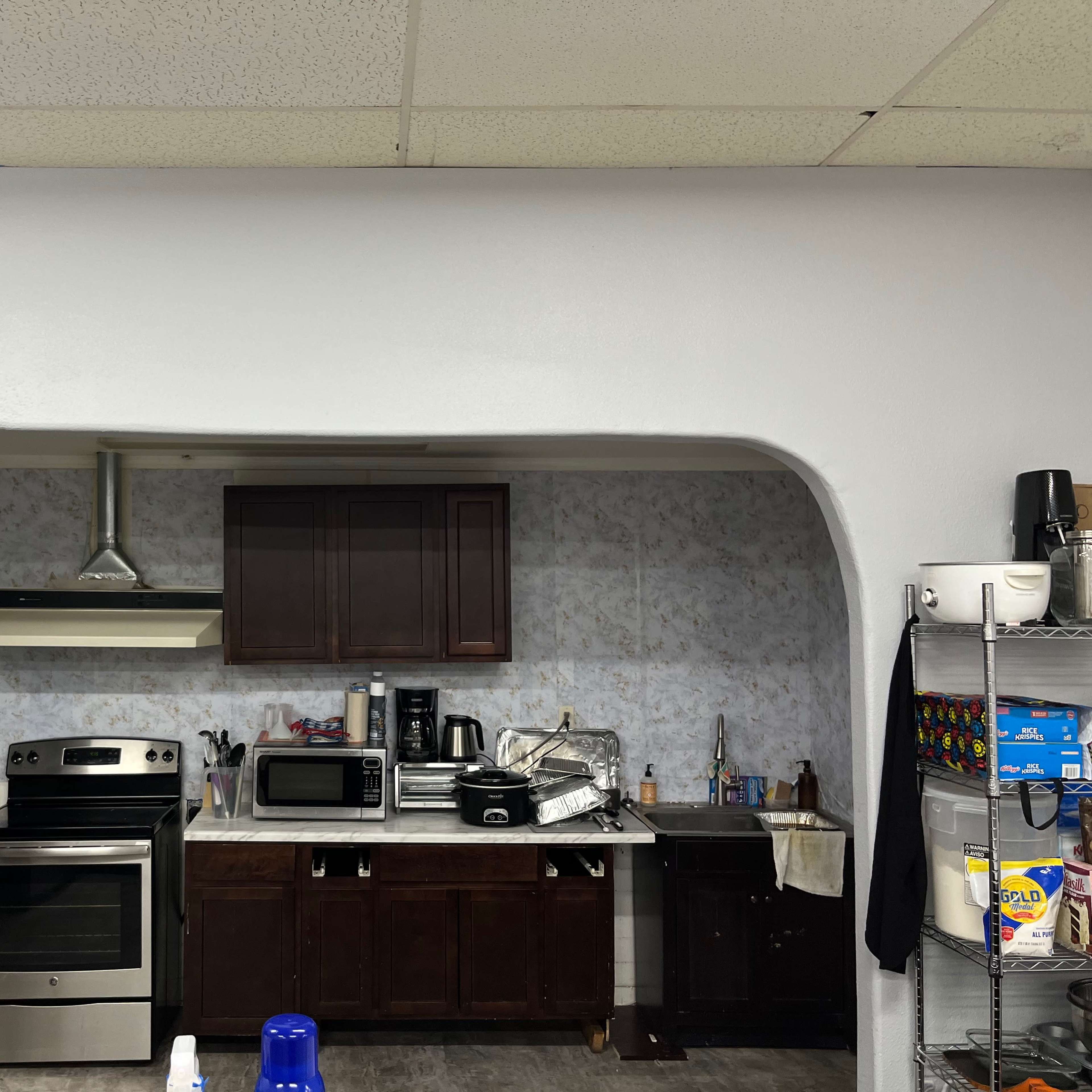 A kitchen with a stove, oven, refrigerator, and countertop appliances arranged under cabinets against a patterned wall.