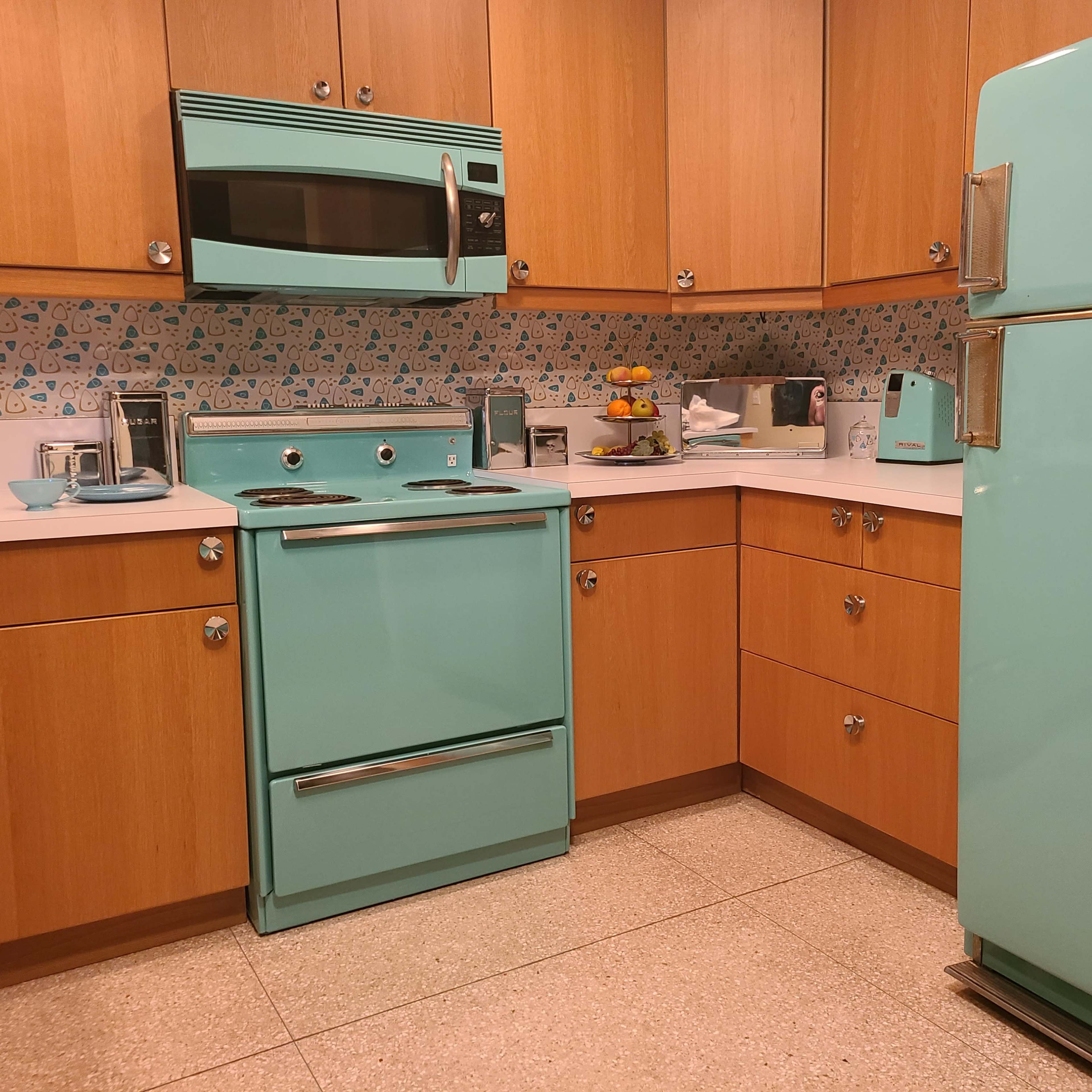 The kitchen features turquoise appliances, wooden cabinets, and a patterned backsplash.