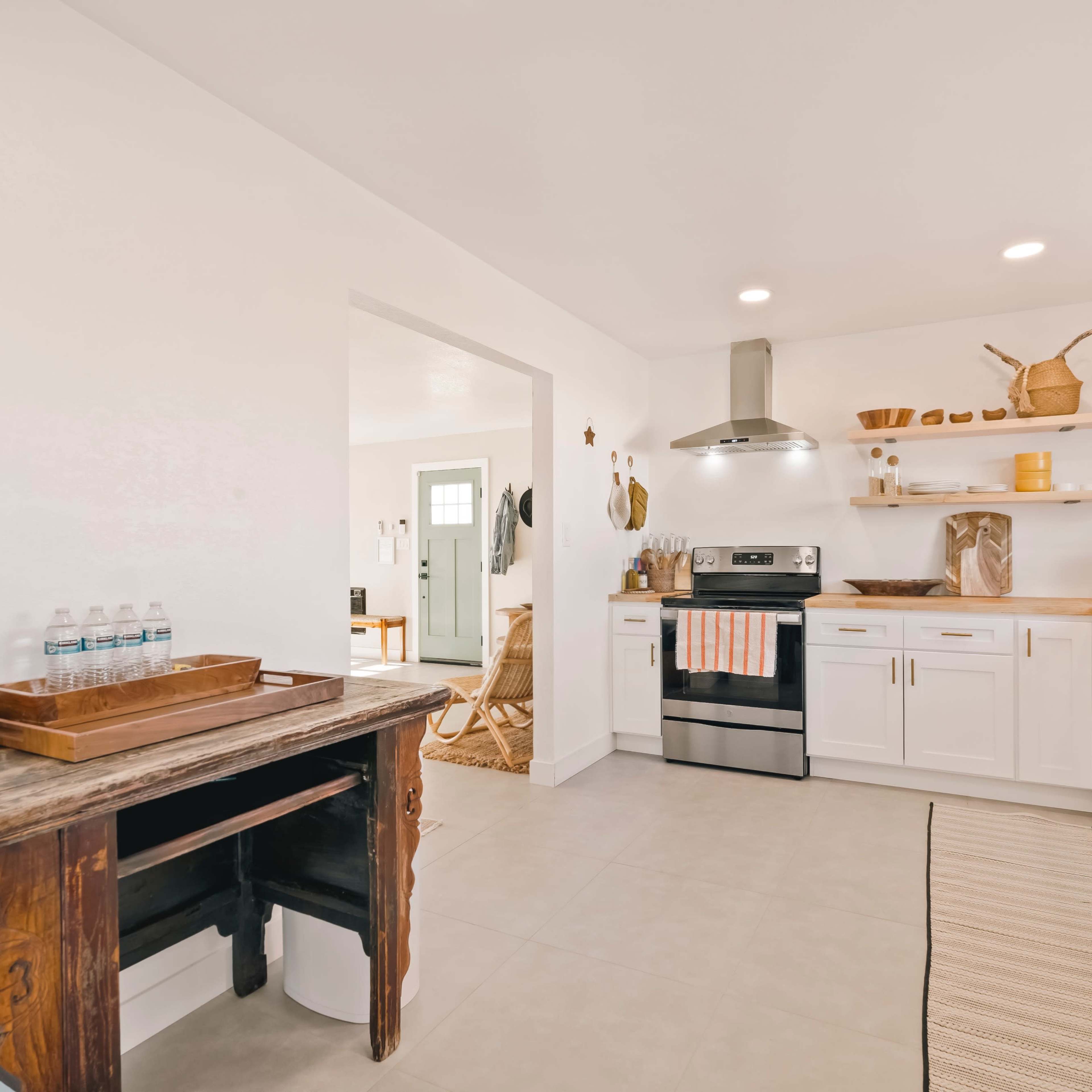A modern kitchen features white cabinetry, stainless steel appliances, and a wooden countertop, with a small dining area visible through an open doorway.
