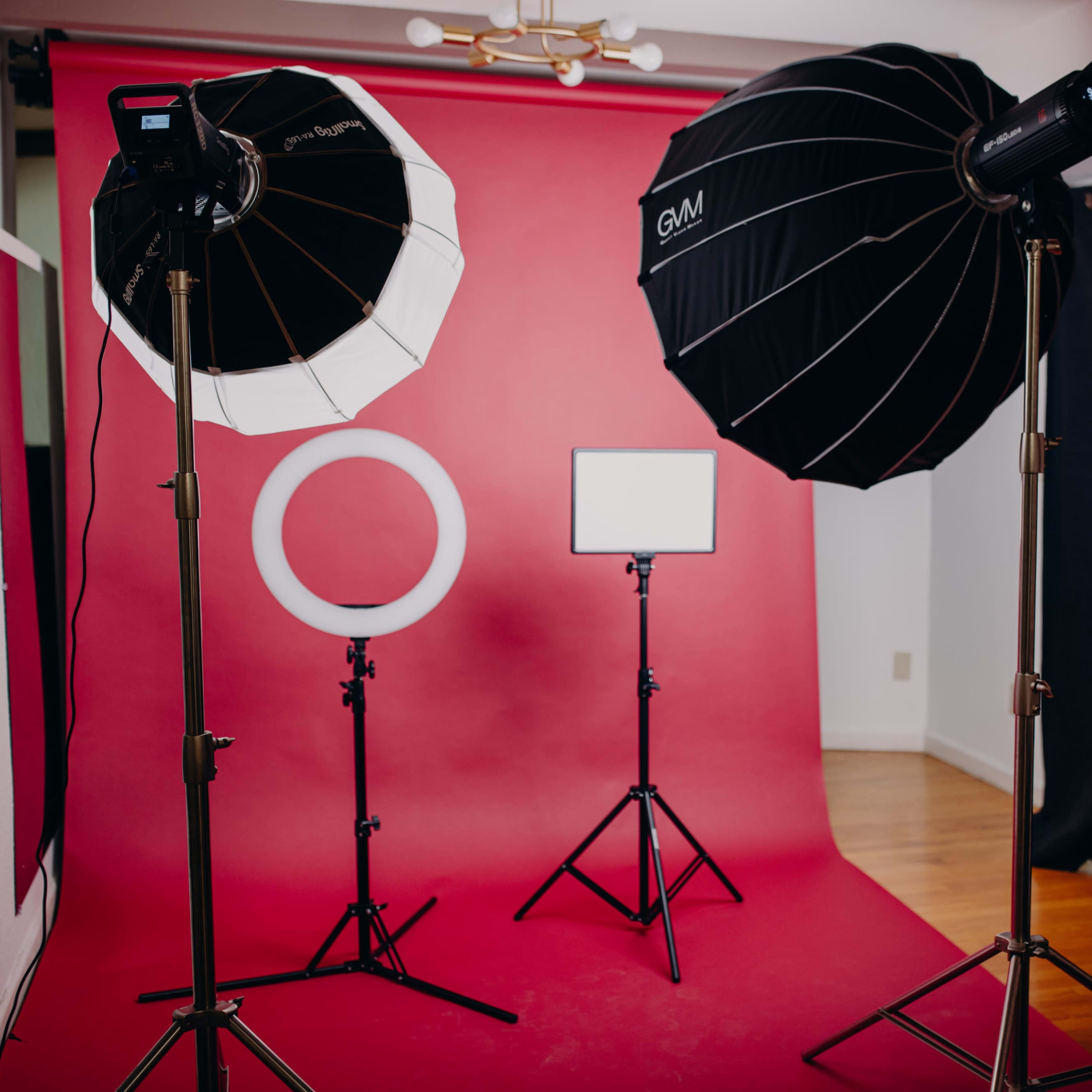 A photography setup with two large softbox lights, a ring light, and a backdrop in vibrant pink.