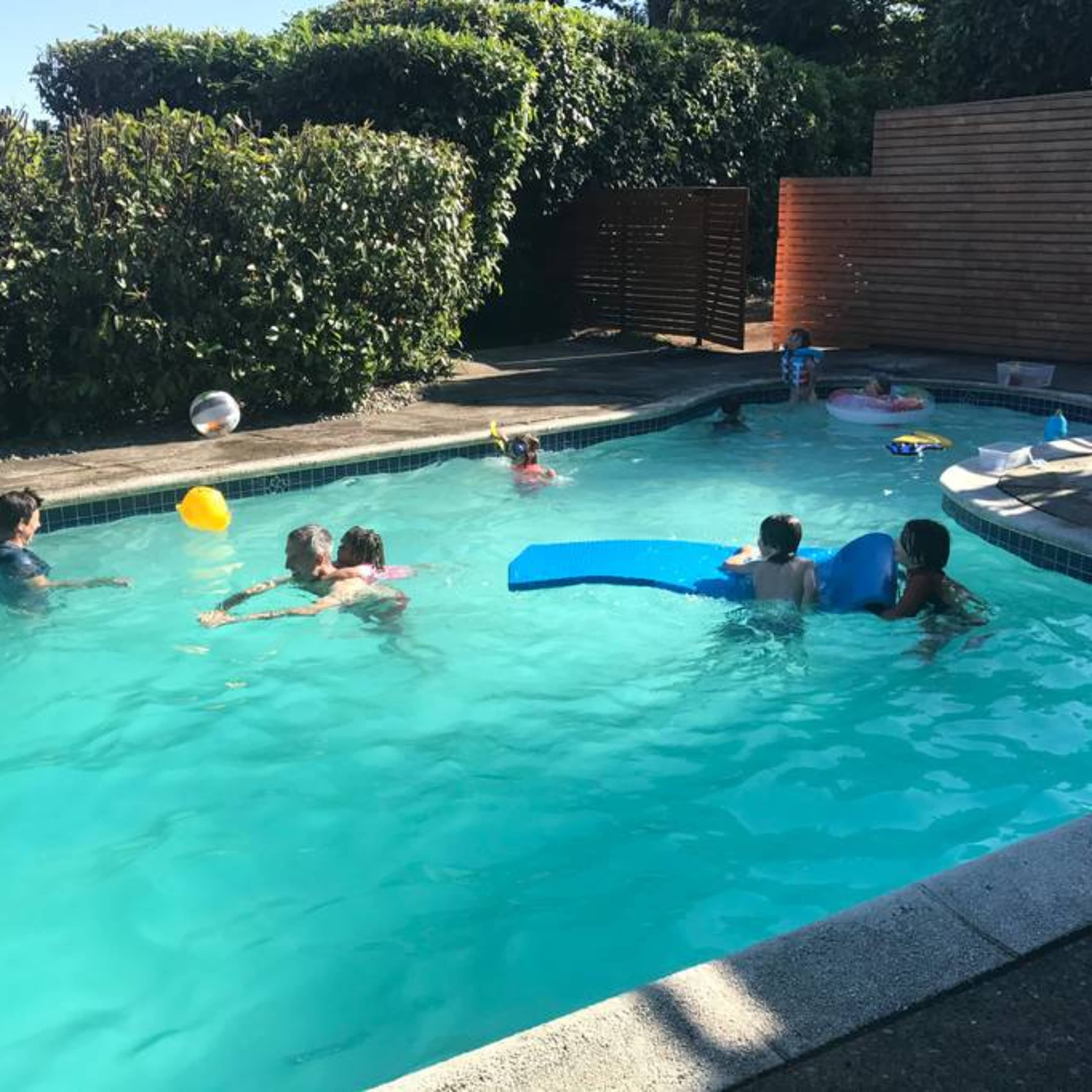 A group of children and adults are playing in a swimming pool surrounded by greenery.
