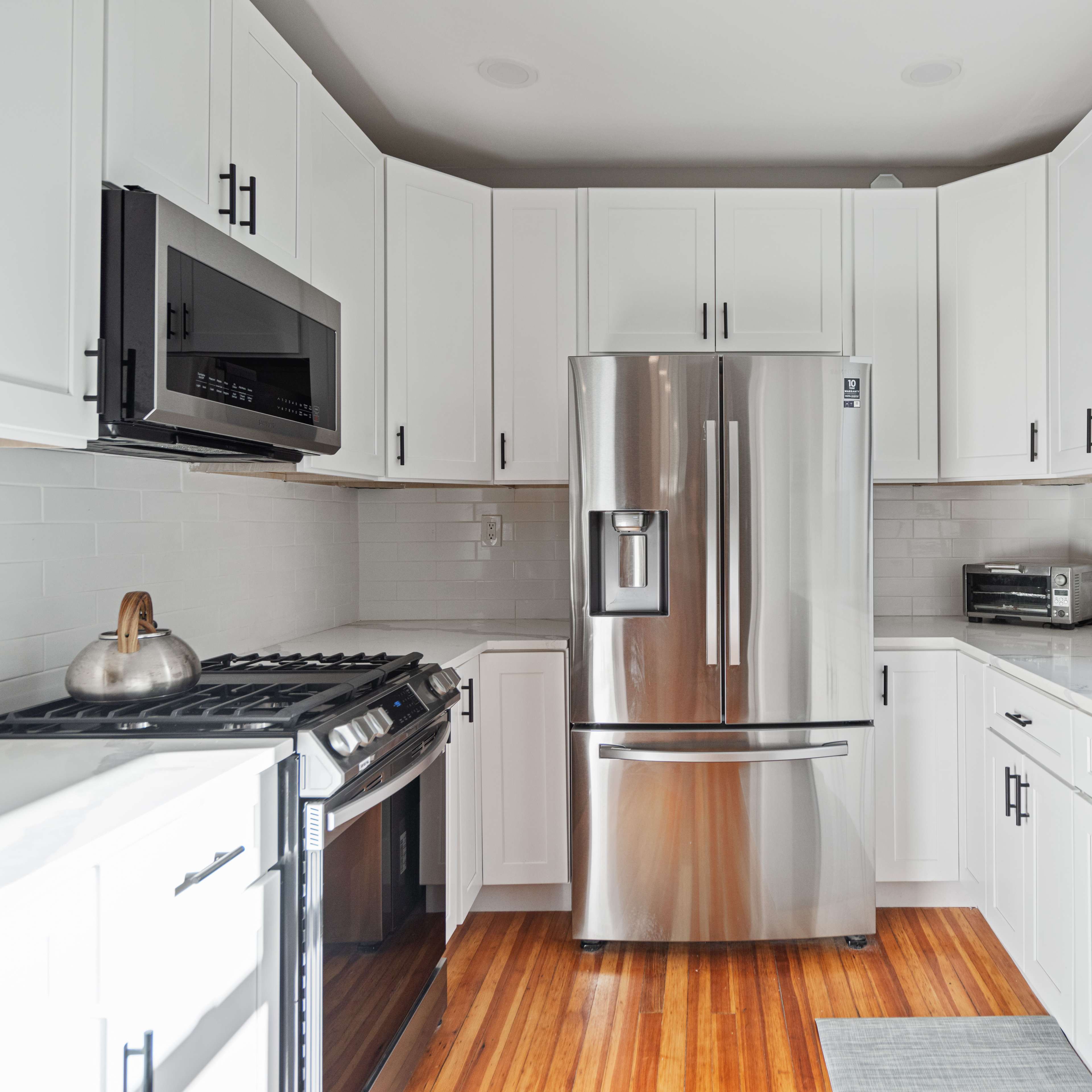 A modern kitchen features white cabinets, stainless steel appliances, and hardwood flooring.