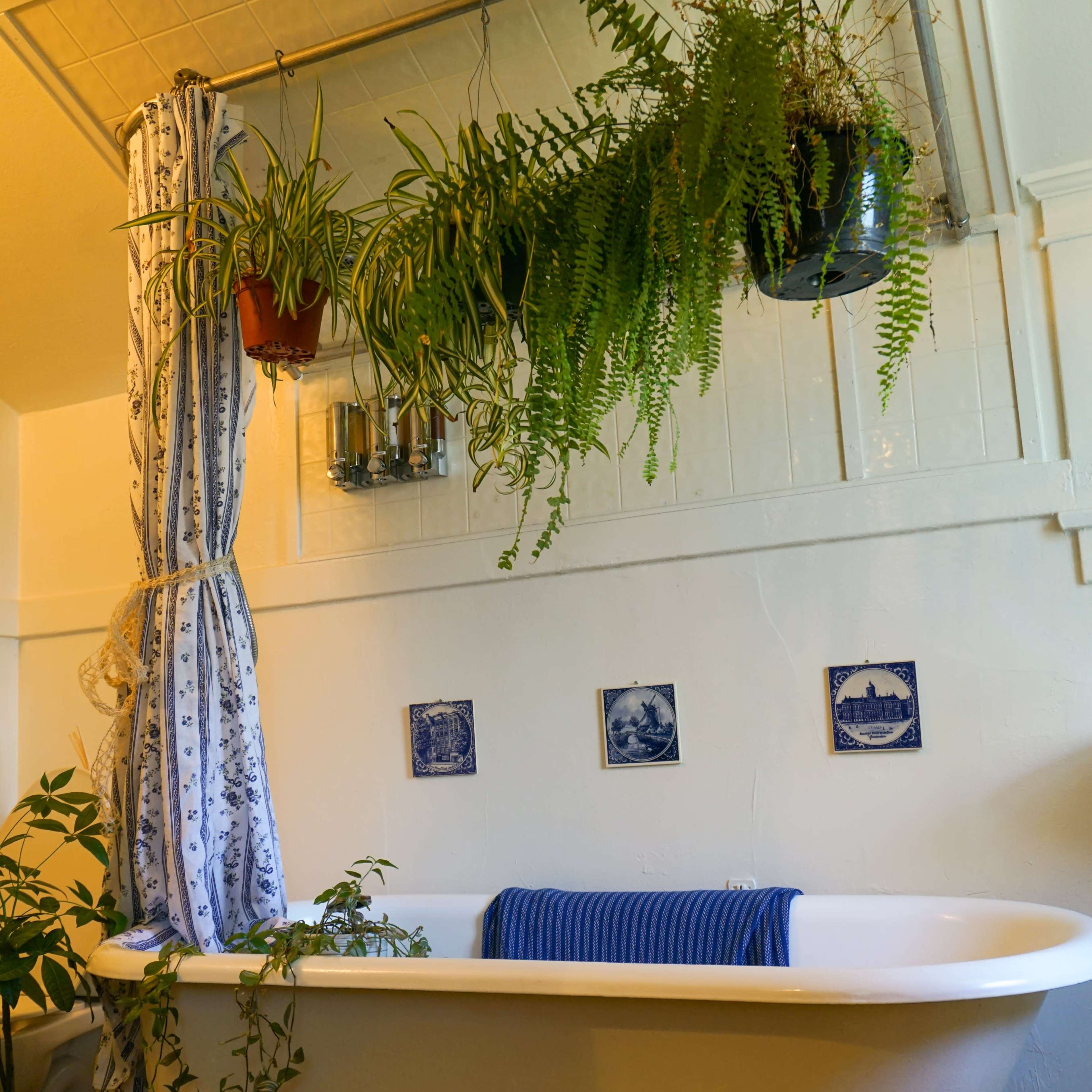 A clawfoot bathtub is positioned against a wall adorned with hanging plants and decorative tiles.