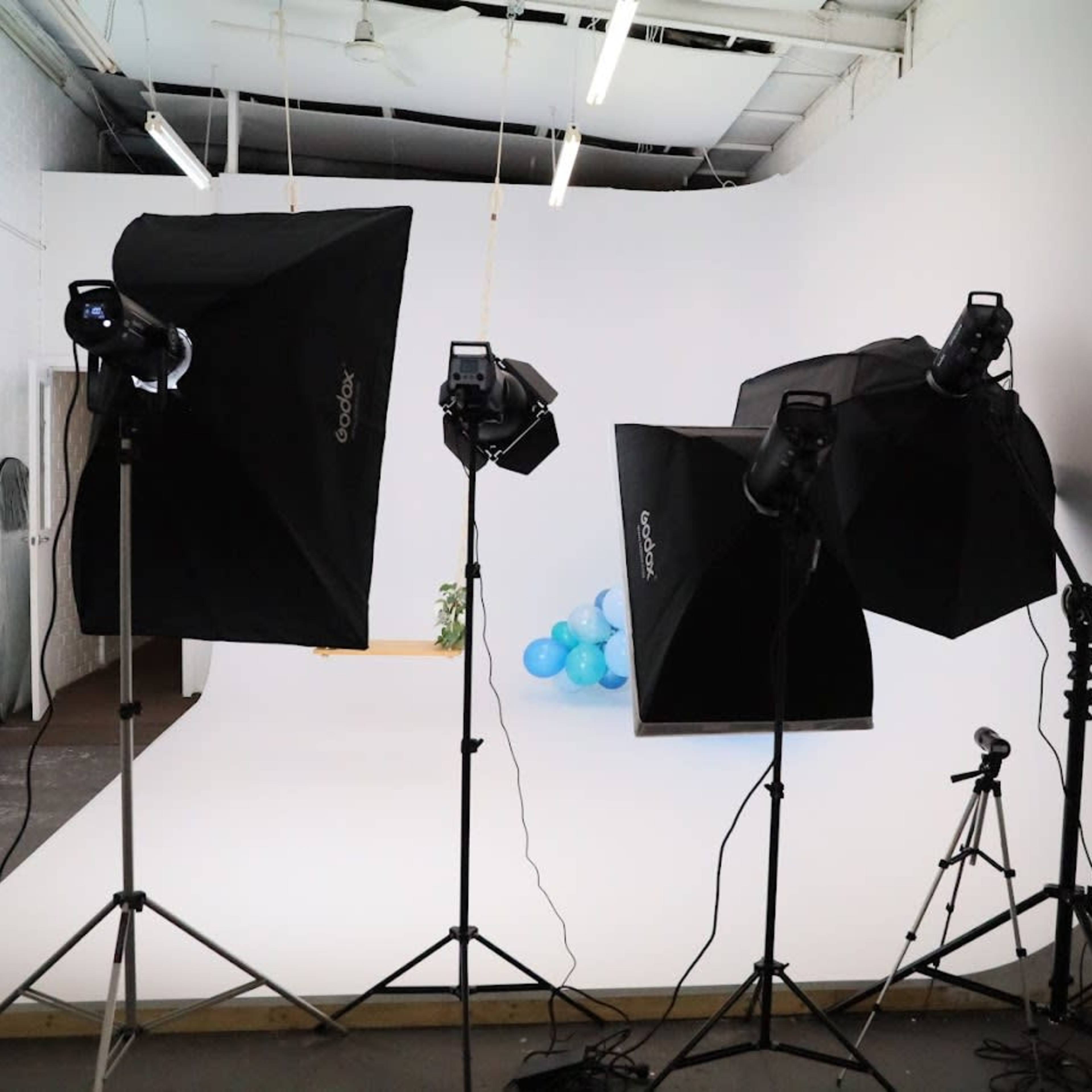 A photography studio setup with three softbox lights, a camera on a tripod, and blue balloons in the background.