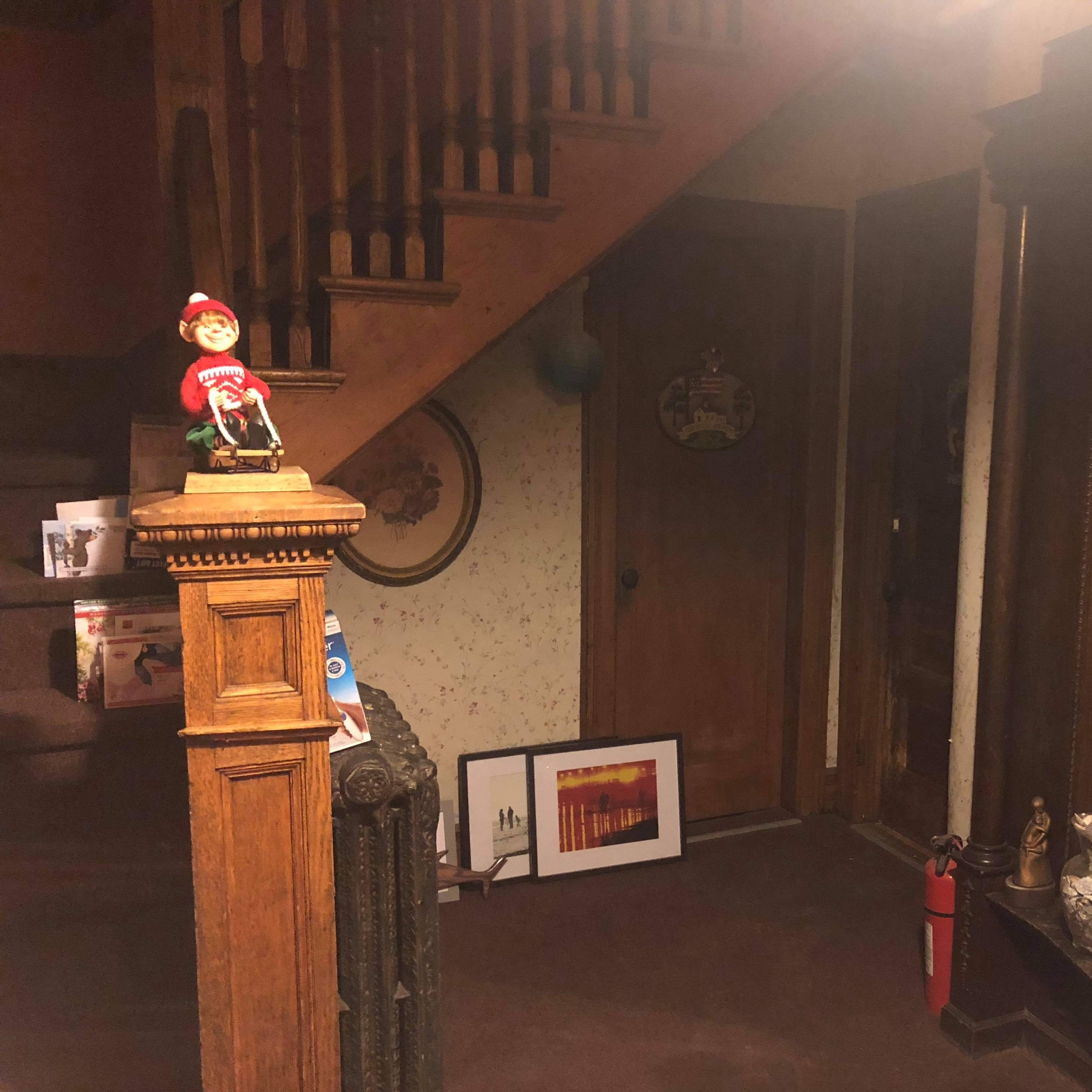 A dimly lit entrance area with a staircase, a wooden banister, and various decorative items displayed along the walls and on furniture.