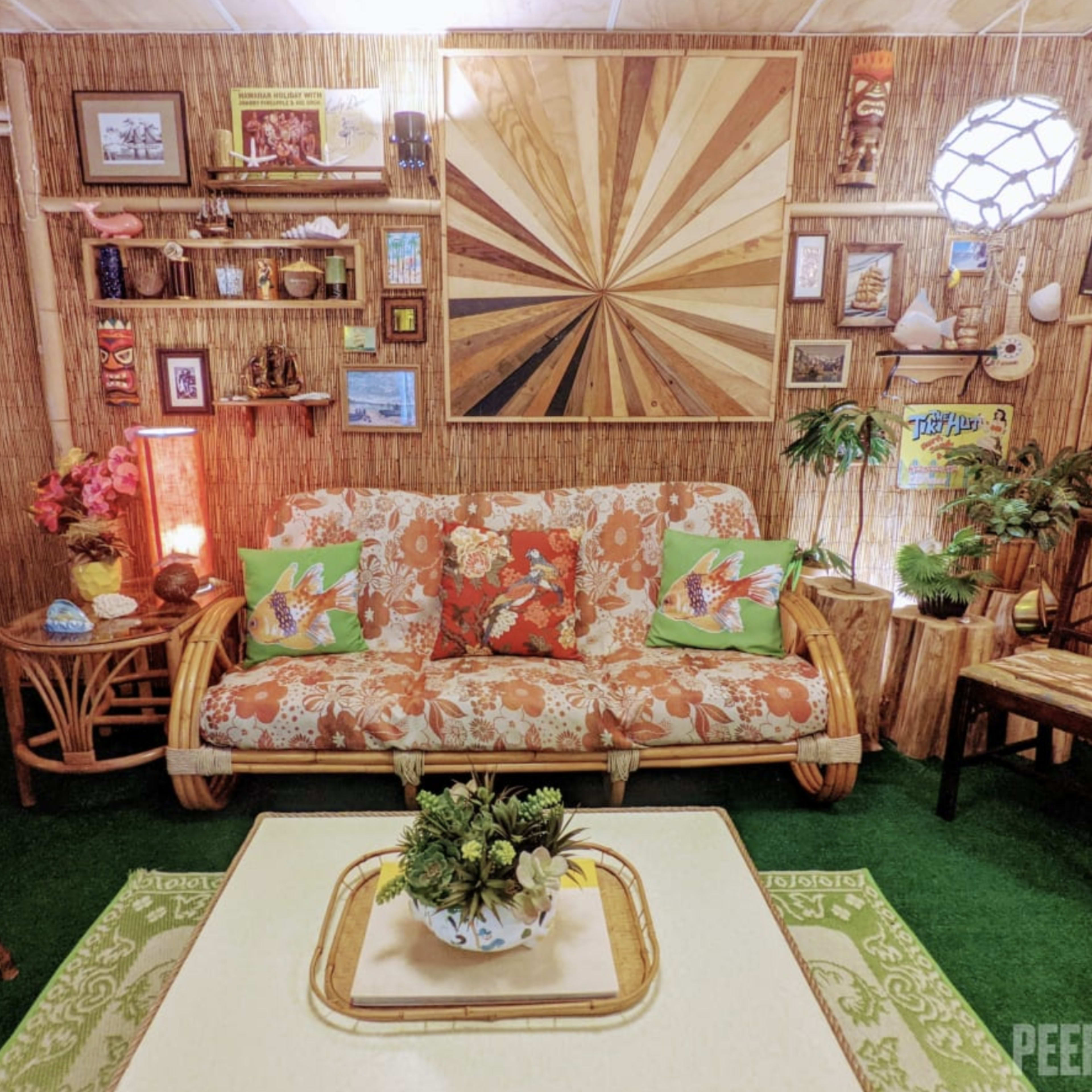 A tropical-themed living room with bamboo decor, a patterned sofa, and various decorative items on the walls.