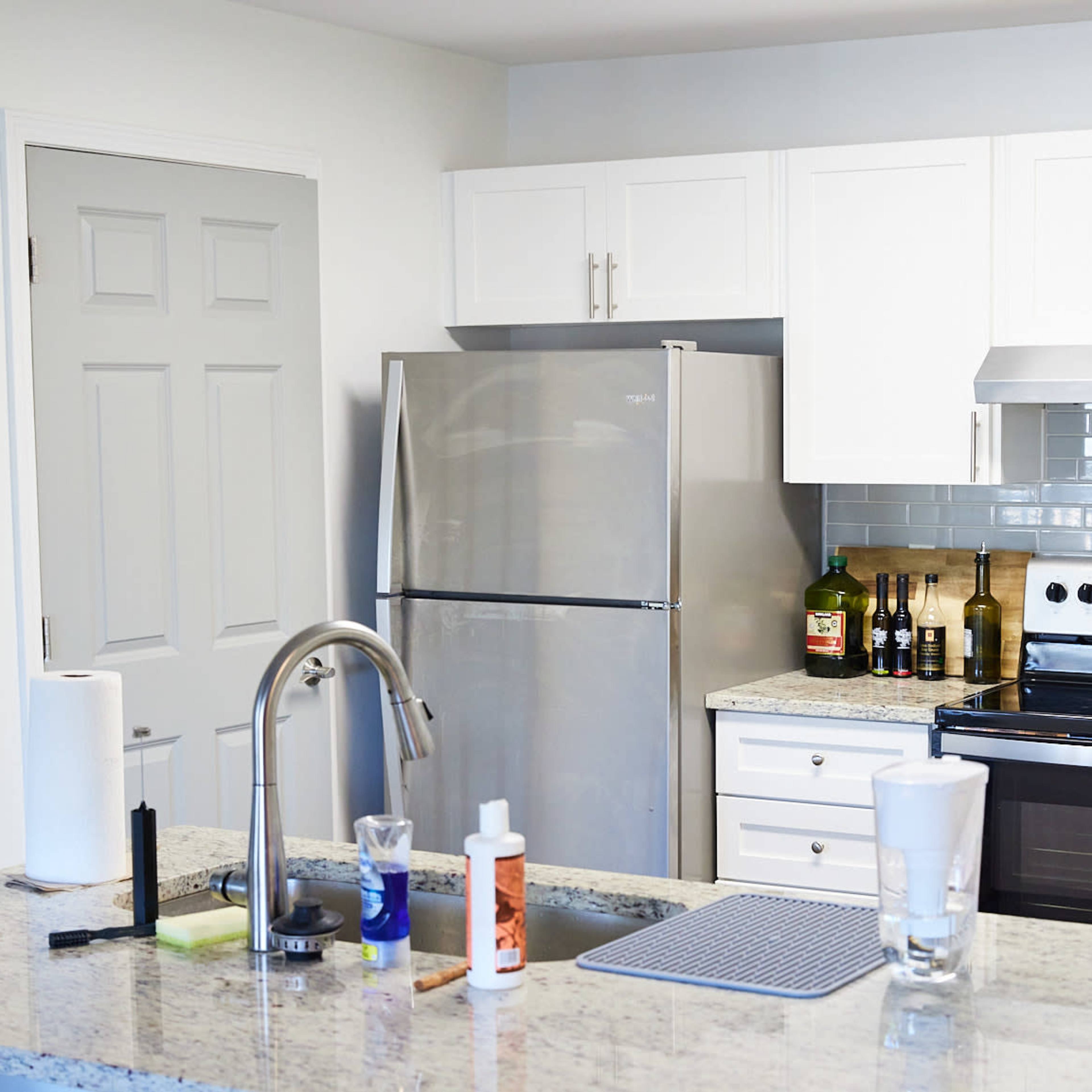 A modern kitchen features a stainless steel refrigerator, an oven, and a countertop with various kitchen items and a sink.