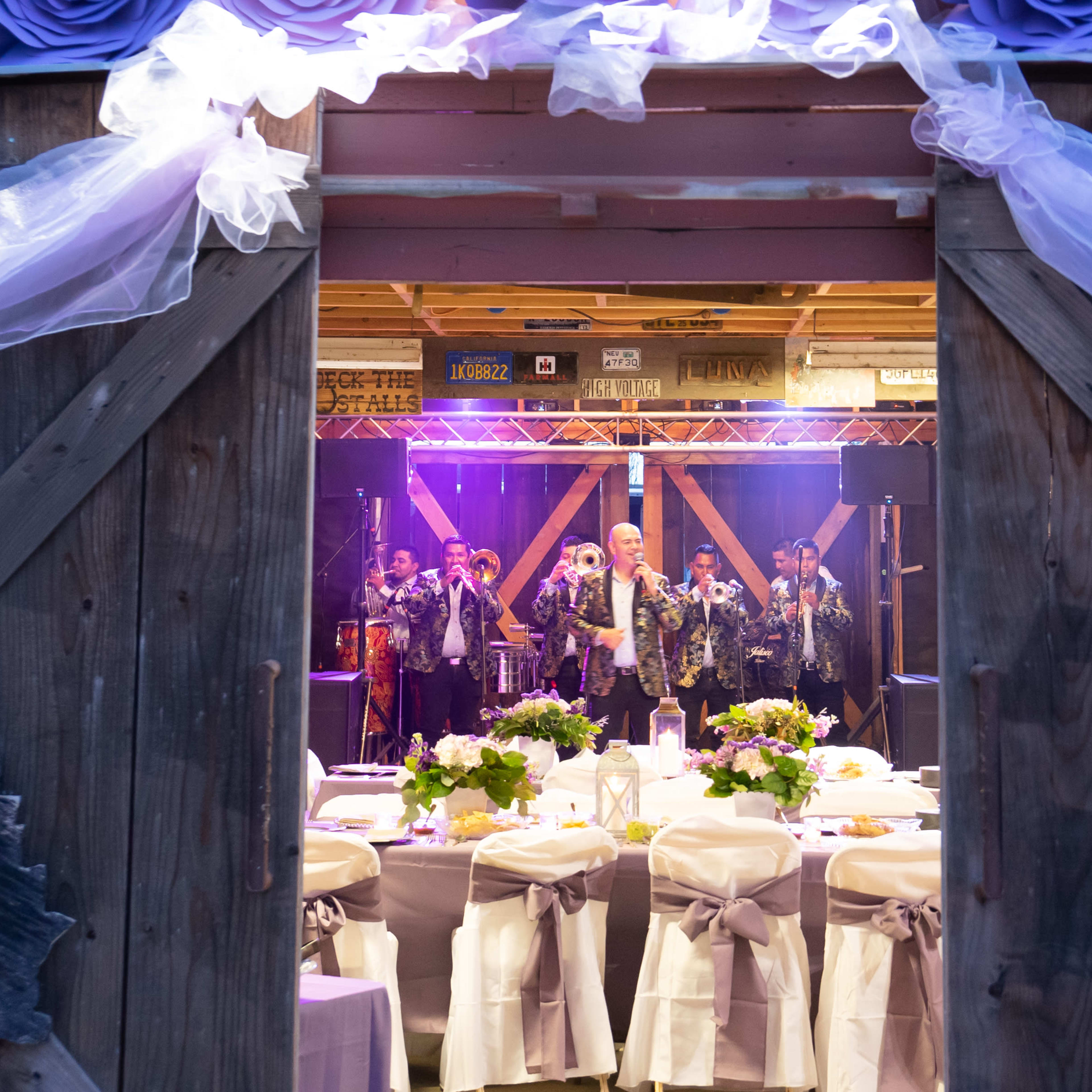 A decorated venue with tables set for a celebration, framed by wooden doors that open to a stage with performers.