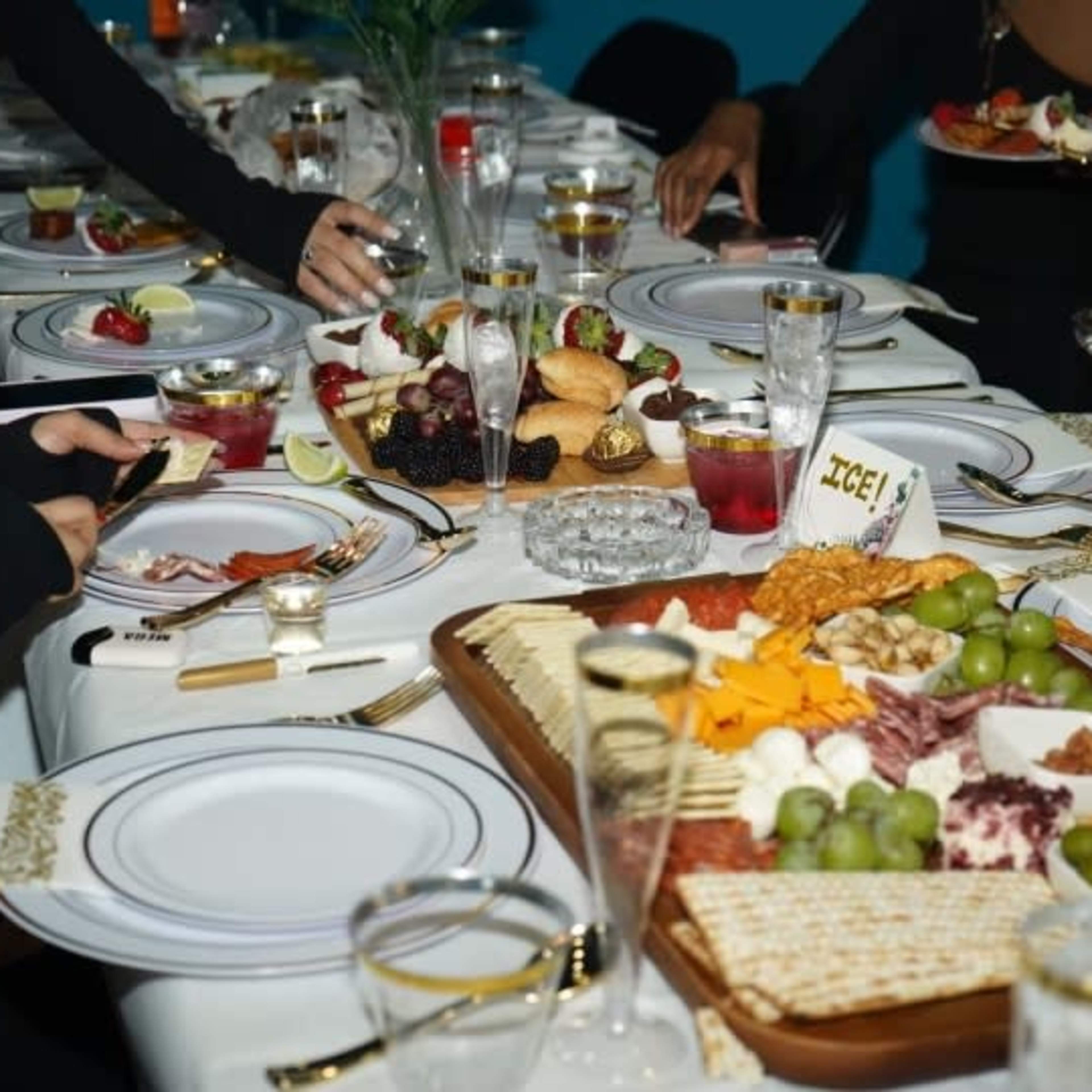The table is set with elegant dishes featuring a variety of foods, including a charcuterie board with fruits, cheeses, and nuts, alongside plates of appetizers and drinks.