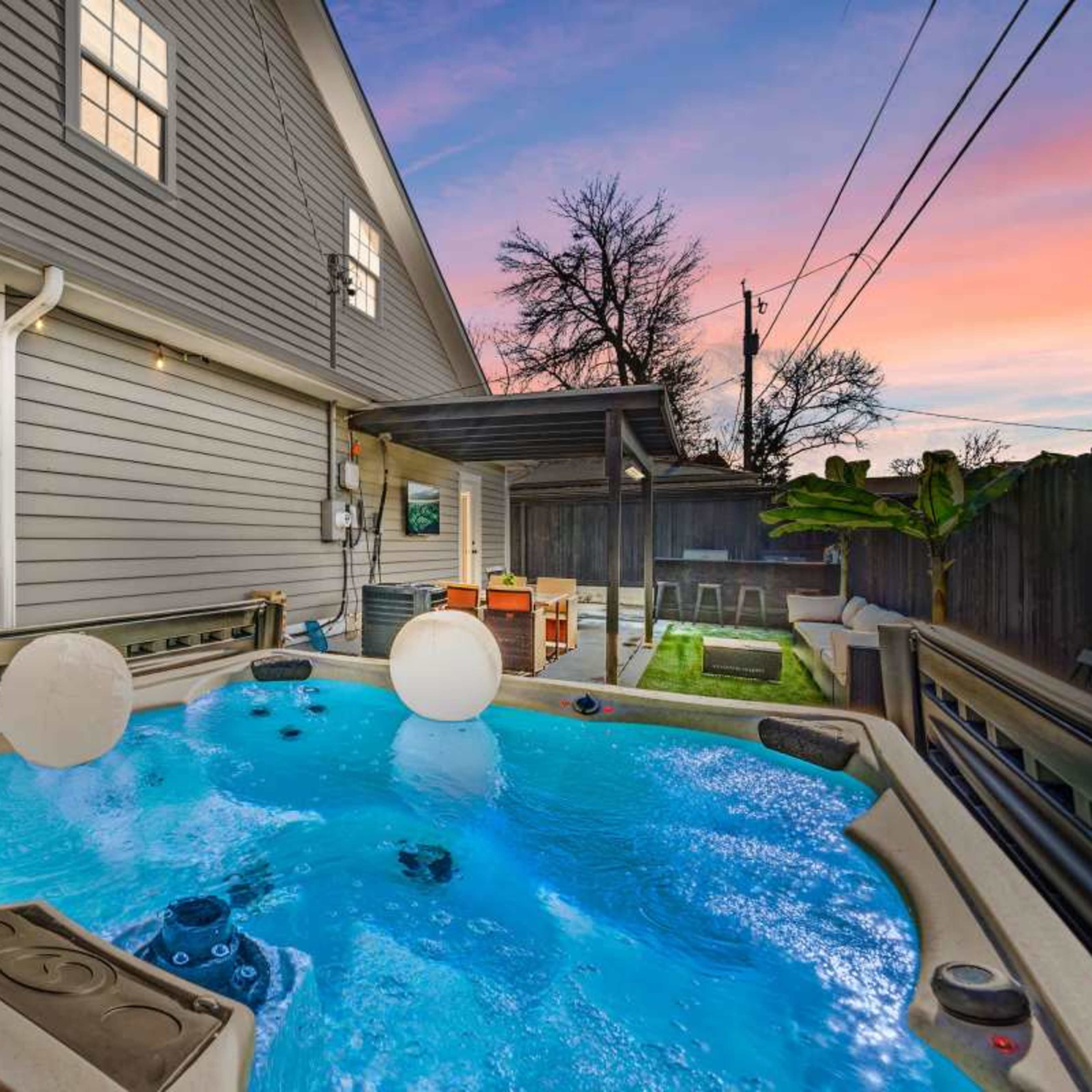 A hot tub with two floating balls in a backyard next to a gray house at twilight.