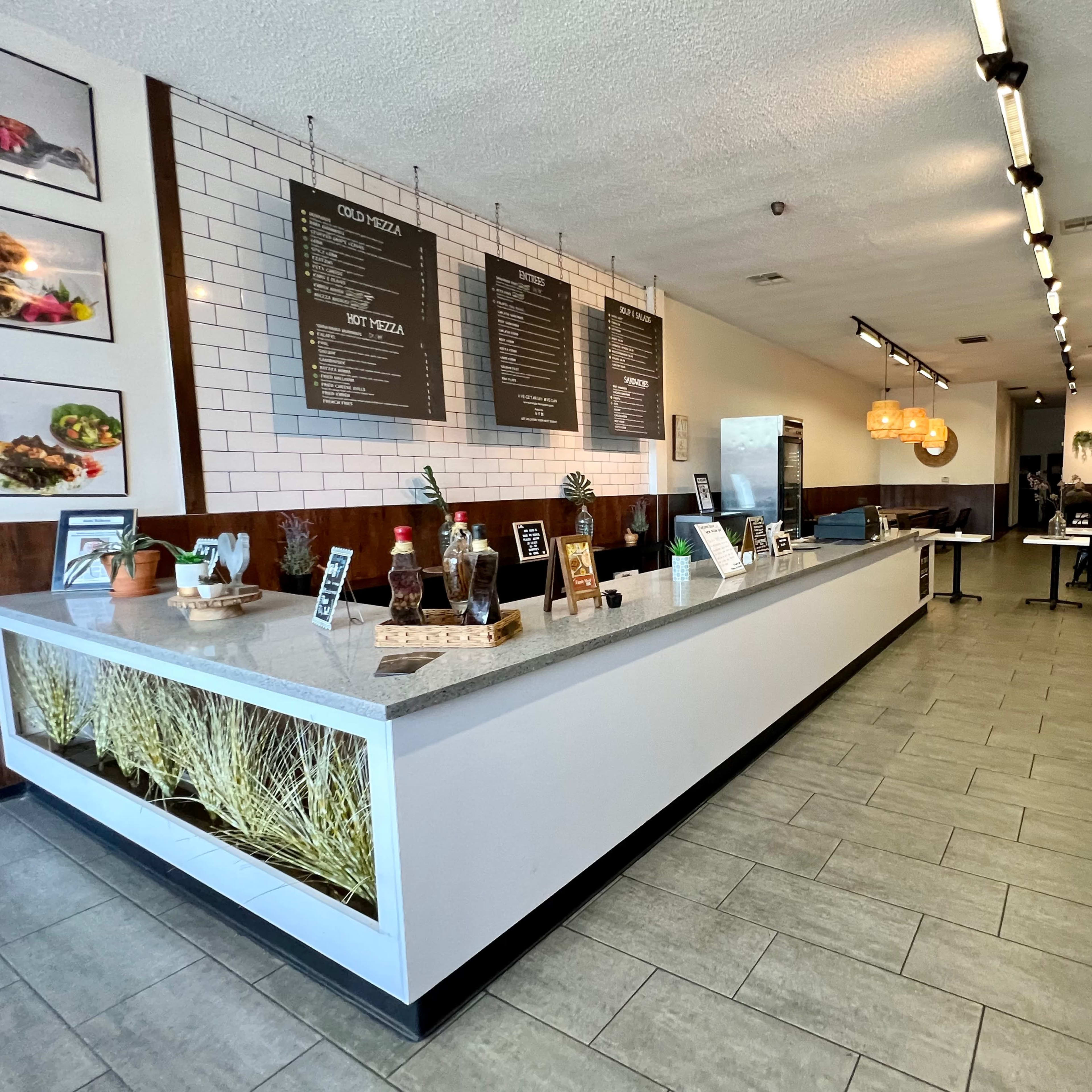 The interior of a modern restaurant features a long service counter with a menu board, and dining tables arranged in an open layout.