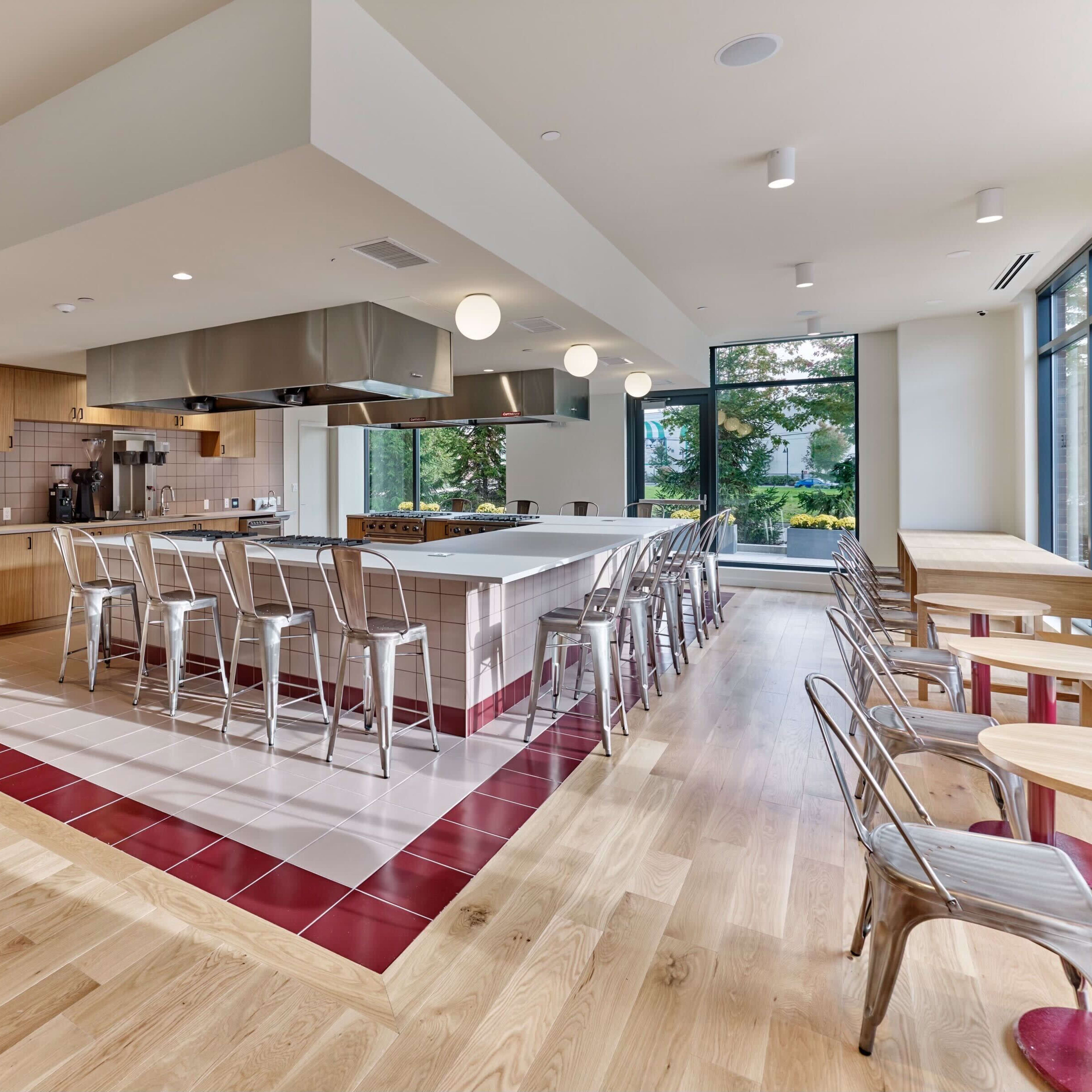 A modern kitchen space with a large central island, stainless steel appliances, and seating at metal bar stools, illuminated by natural light from large windows.