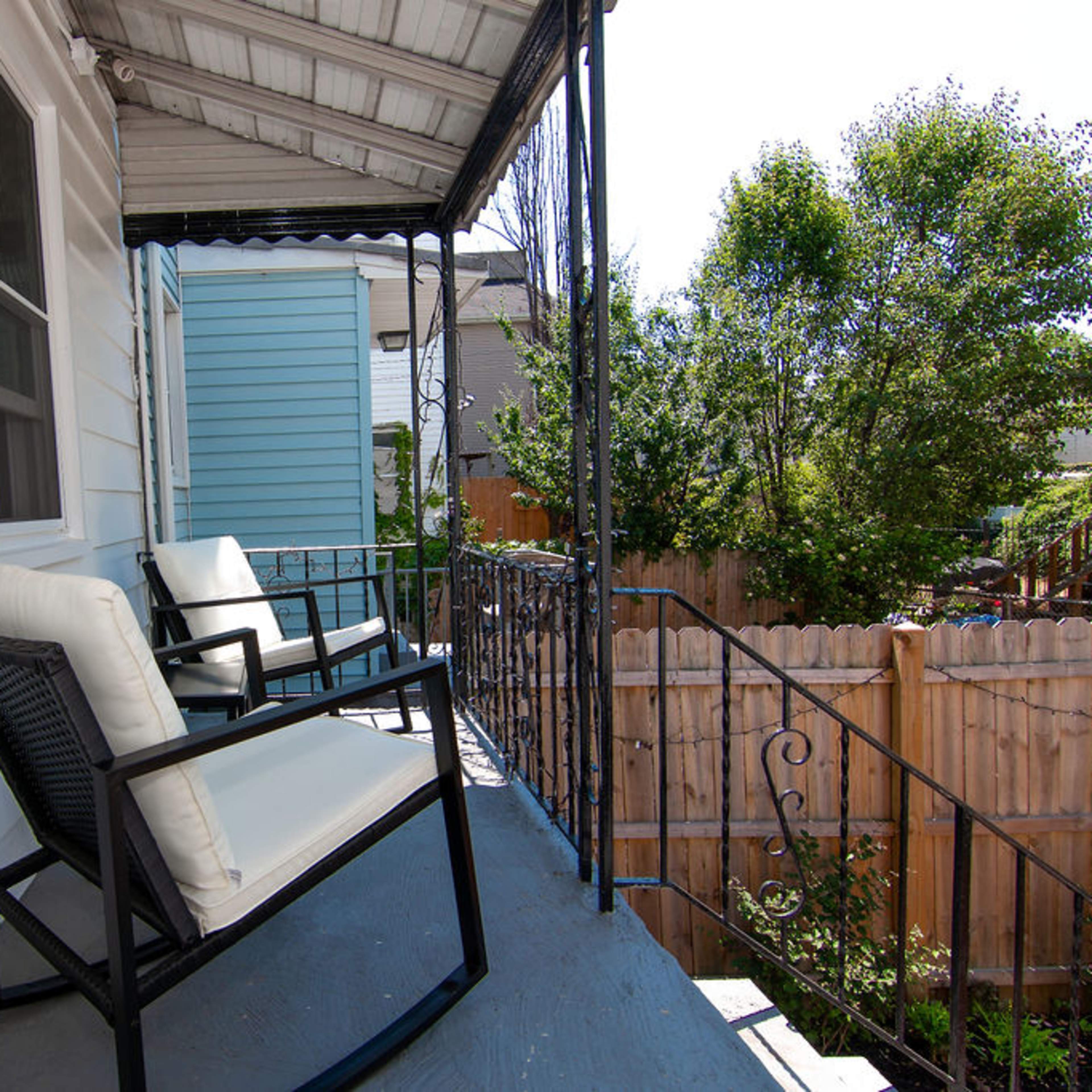 A porch featuring two black chairs with white cushions, overlooking a fenced yard and neighboring houses.