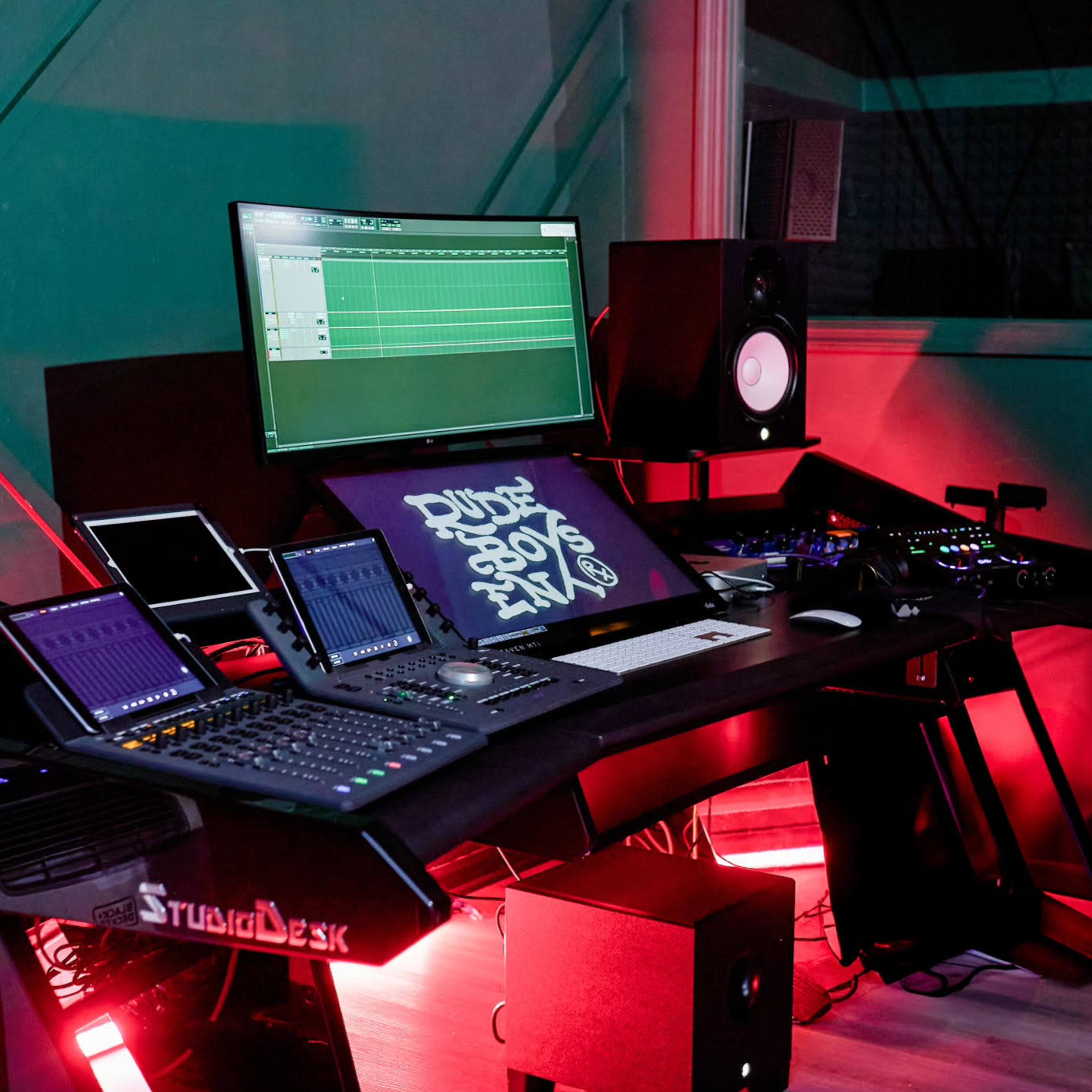 A modern music production studio featuring a large desk with audio mixing equipment, computer screens, and speakers.