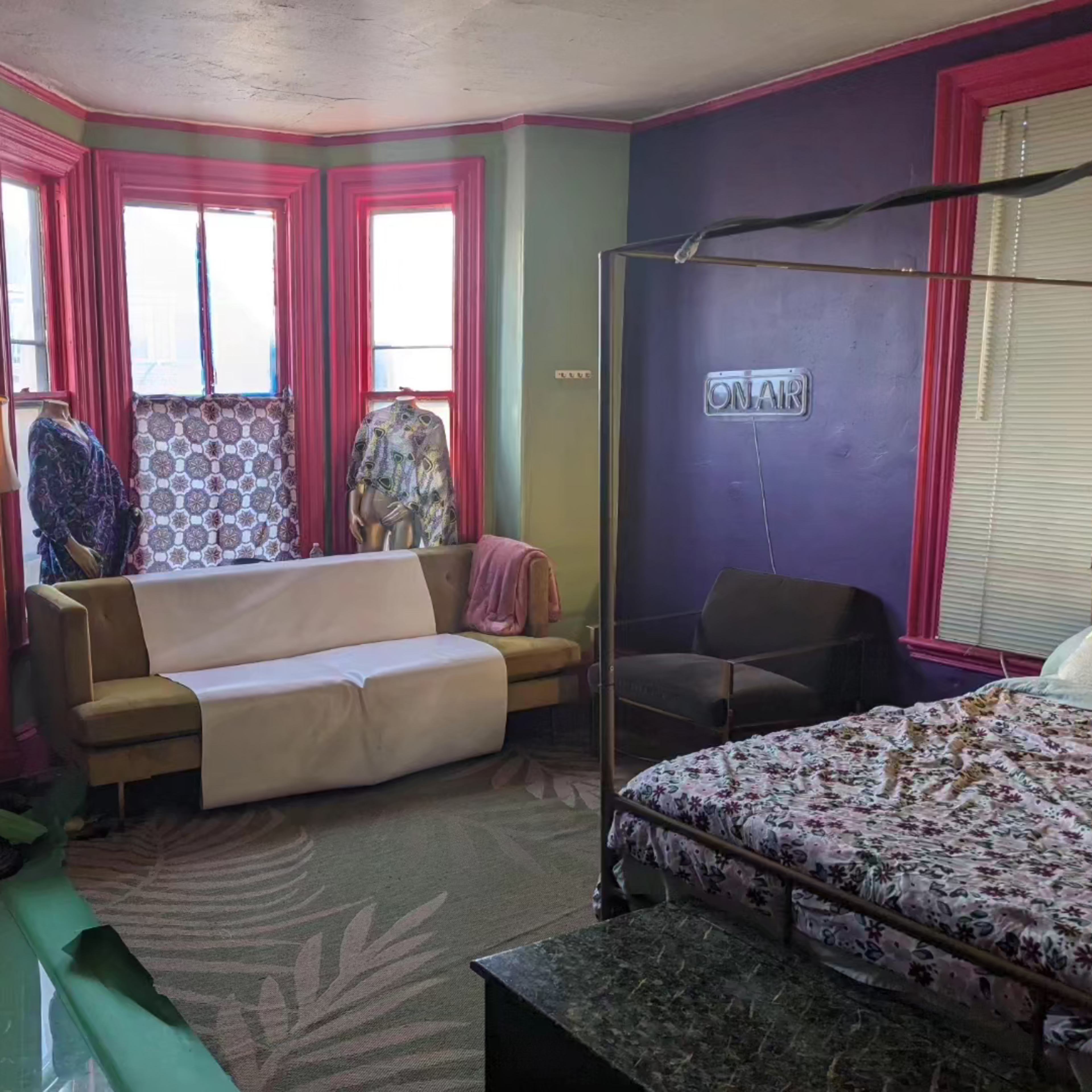 A colorful room featuring a bed with a patterned cover, a sofa partially covered with a white cloth, and a lamp beside a window.