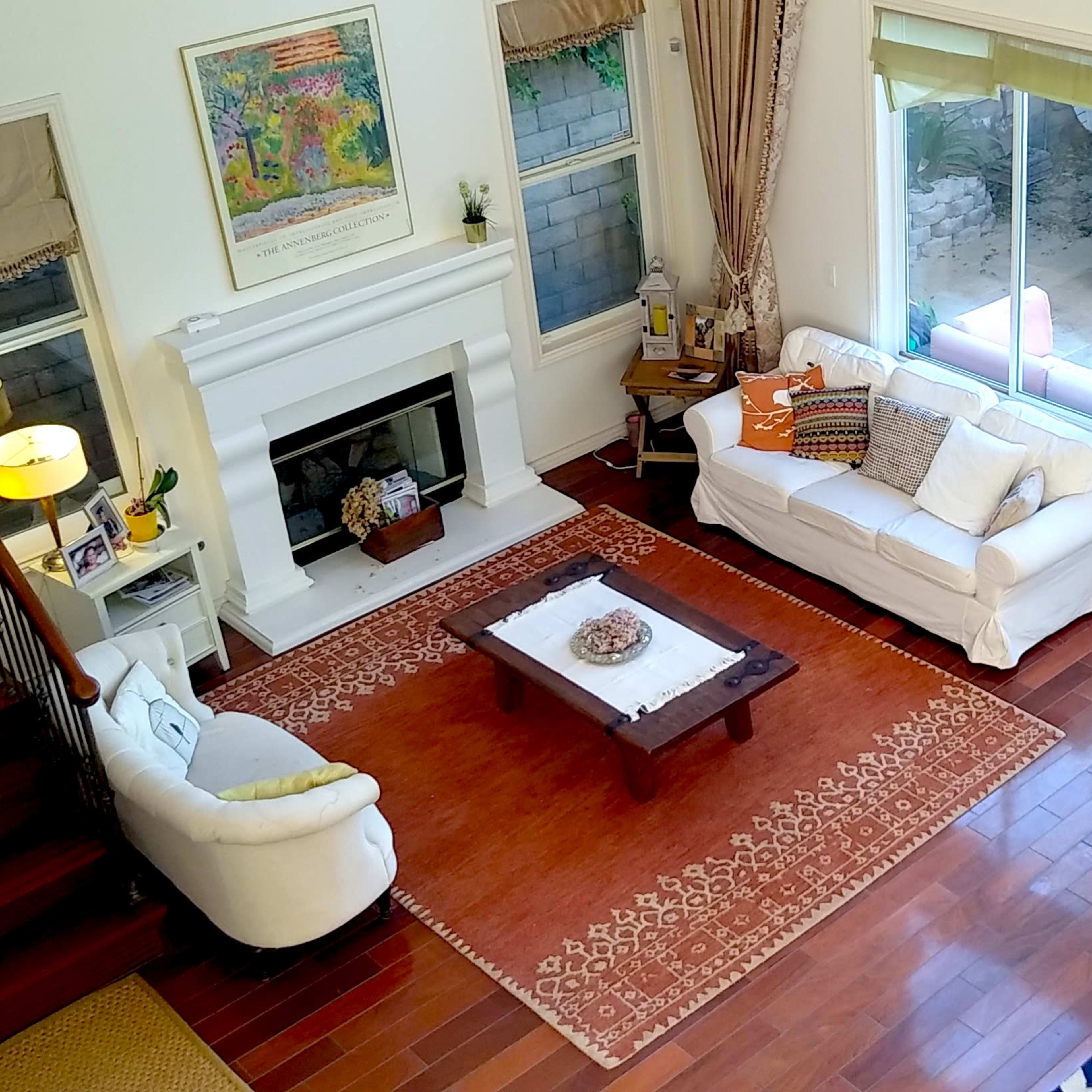 A spacious living area with a fireplace, a white sofa, and a dining table, featuring large windows that overlook an outdoor space.