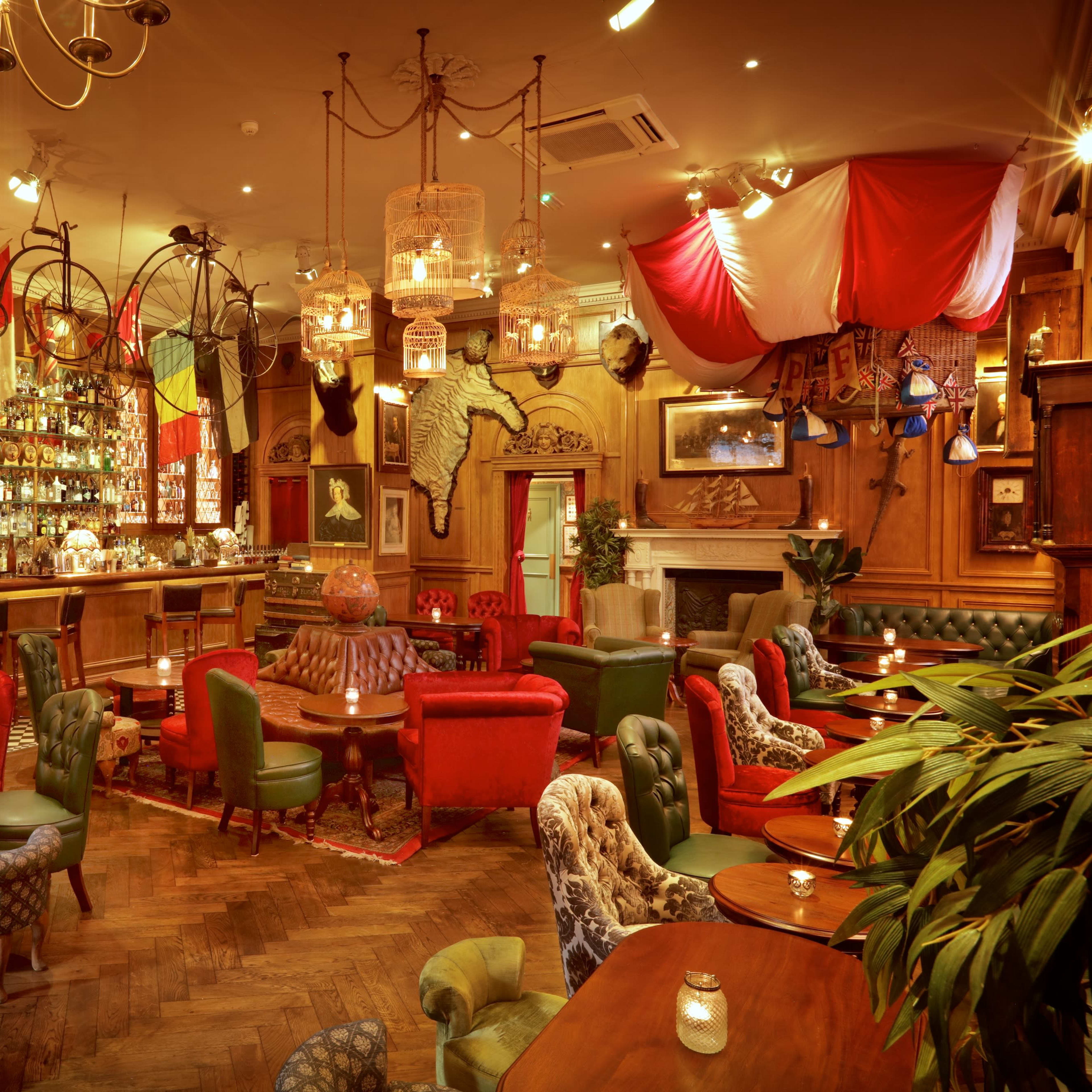 A cozy bar interior with a mix of colorful upholstered chairs, wooden beams, and a well-stocked bar in the background.