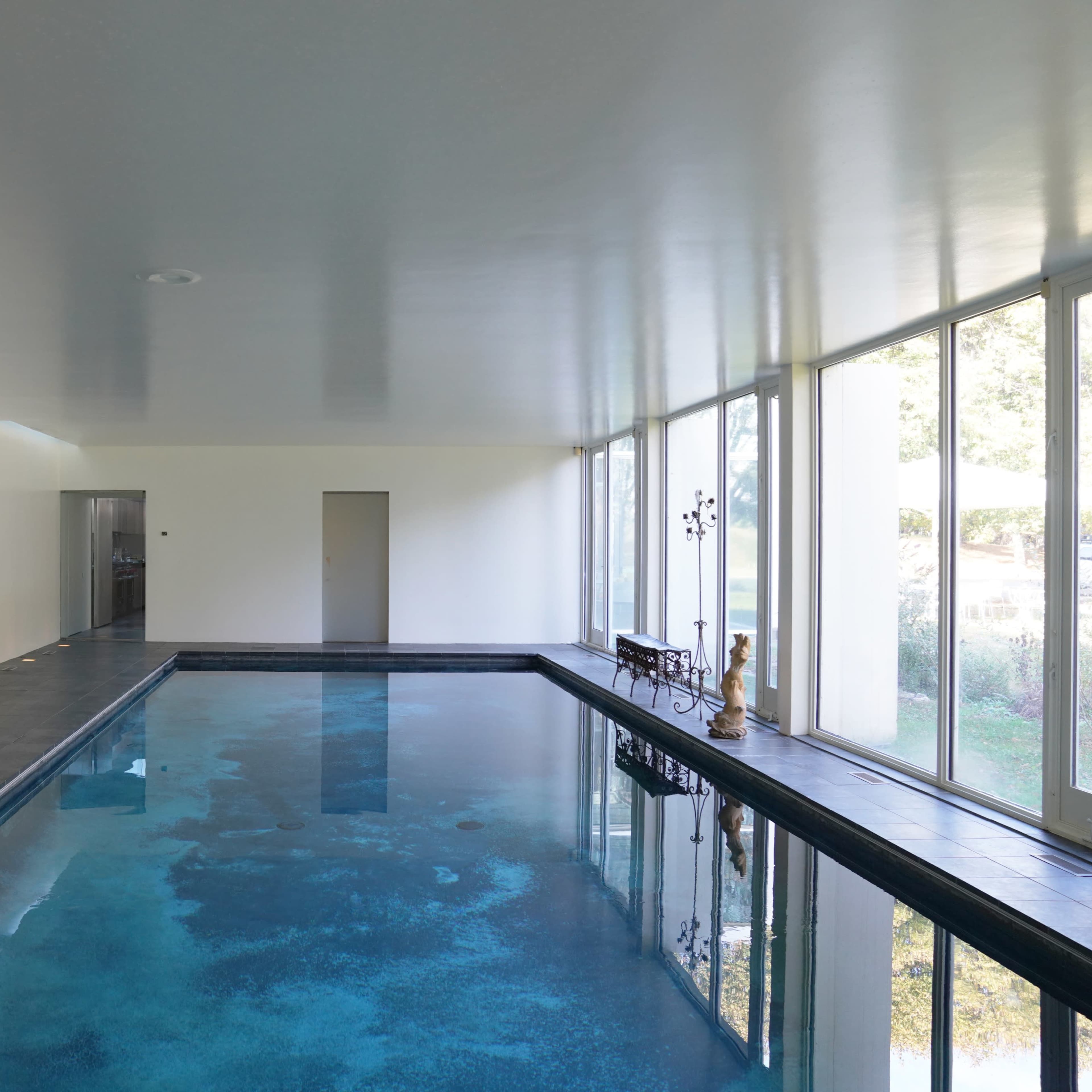 An indoor swimming pool with a tiled edge and large windows allowing natural light to enter.
