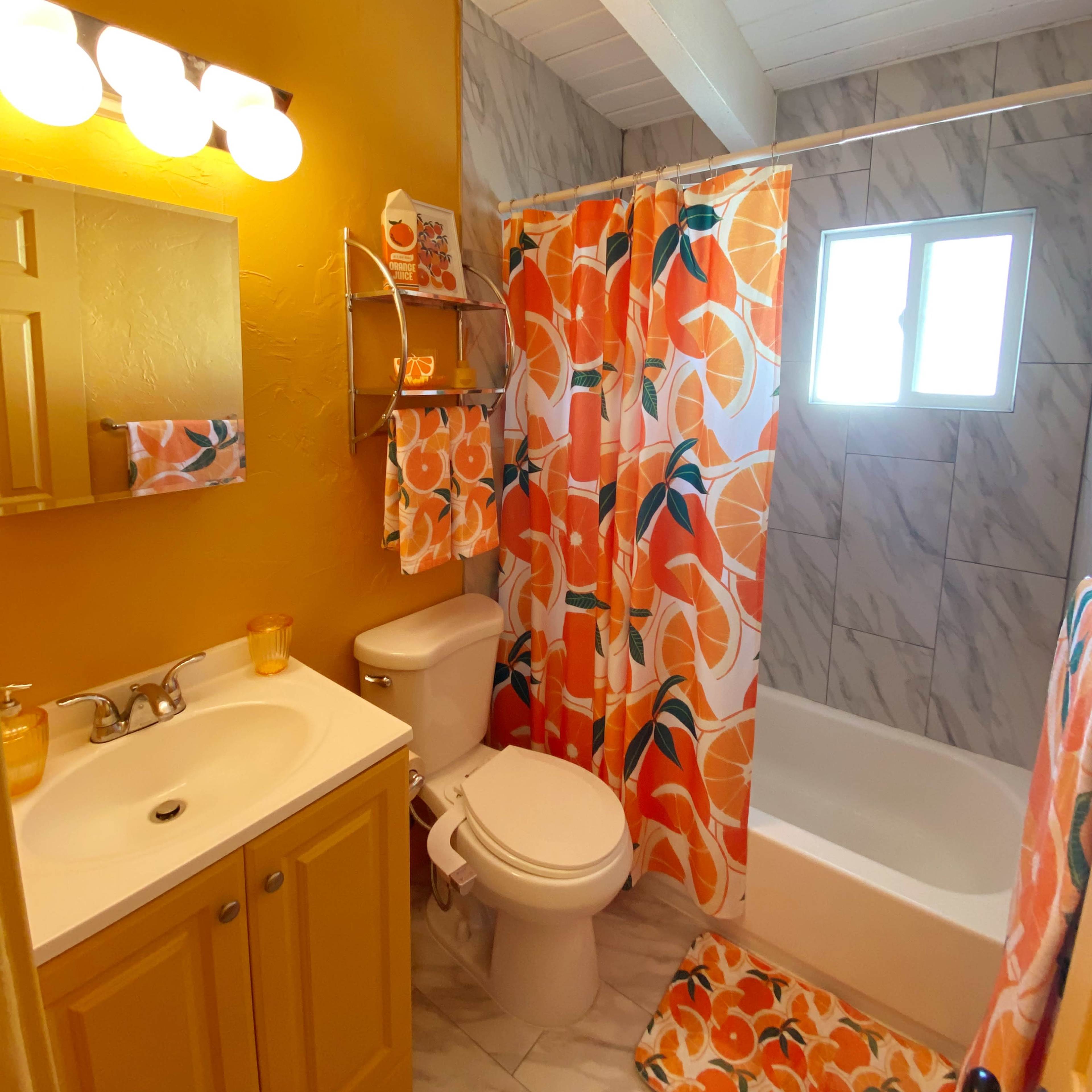 A small bathroom featuring yellow walls, a white bathtub, a white toilet, and a shower curtain with a vibrant orange floral pattern.