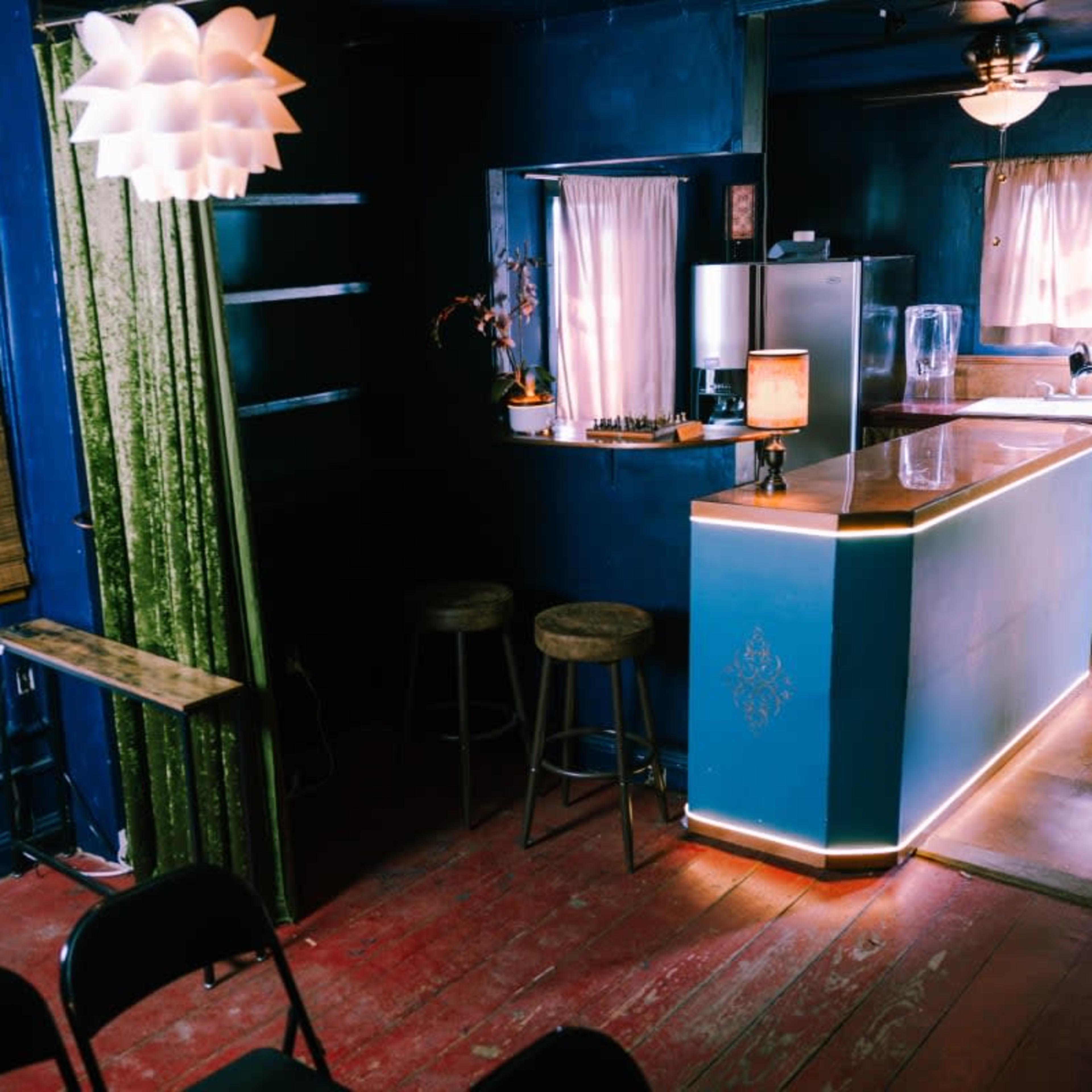 A cozy interior room featuring a bar with stools, a kitchen area, an AC unit, and a distinctive overhead light fixture, all set against deep blue walls.
