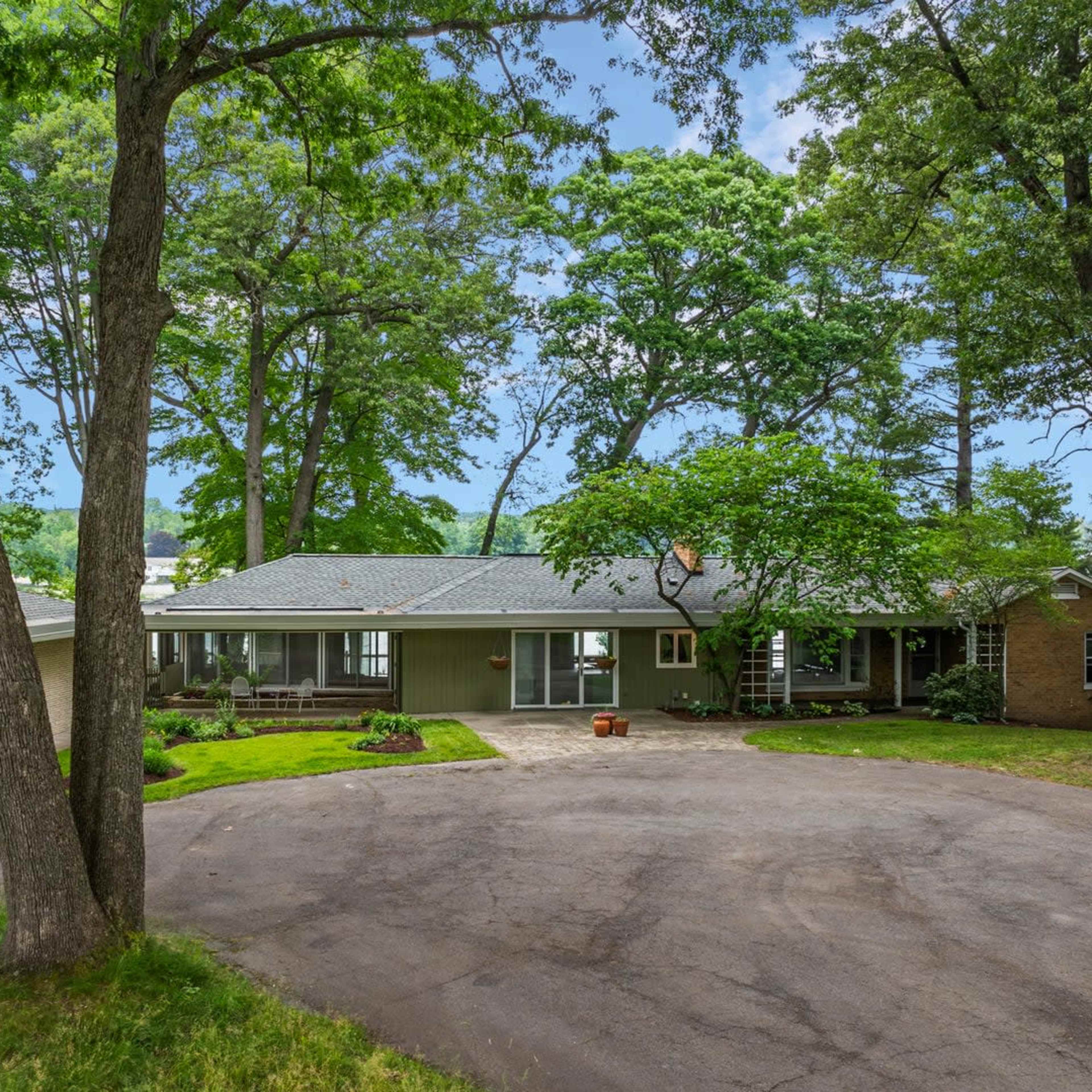 A single-story house with a landscaped front yard and a circular driveway surrounded by trees.