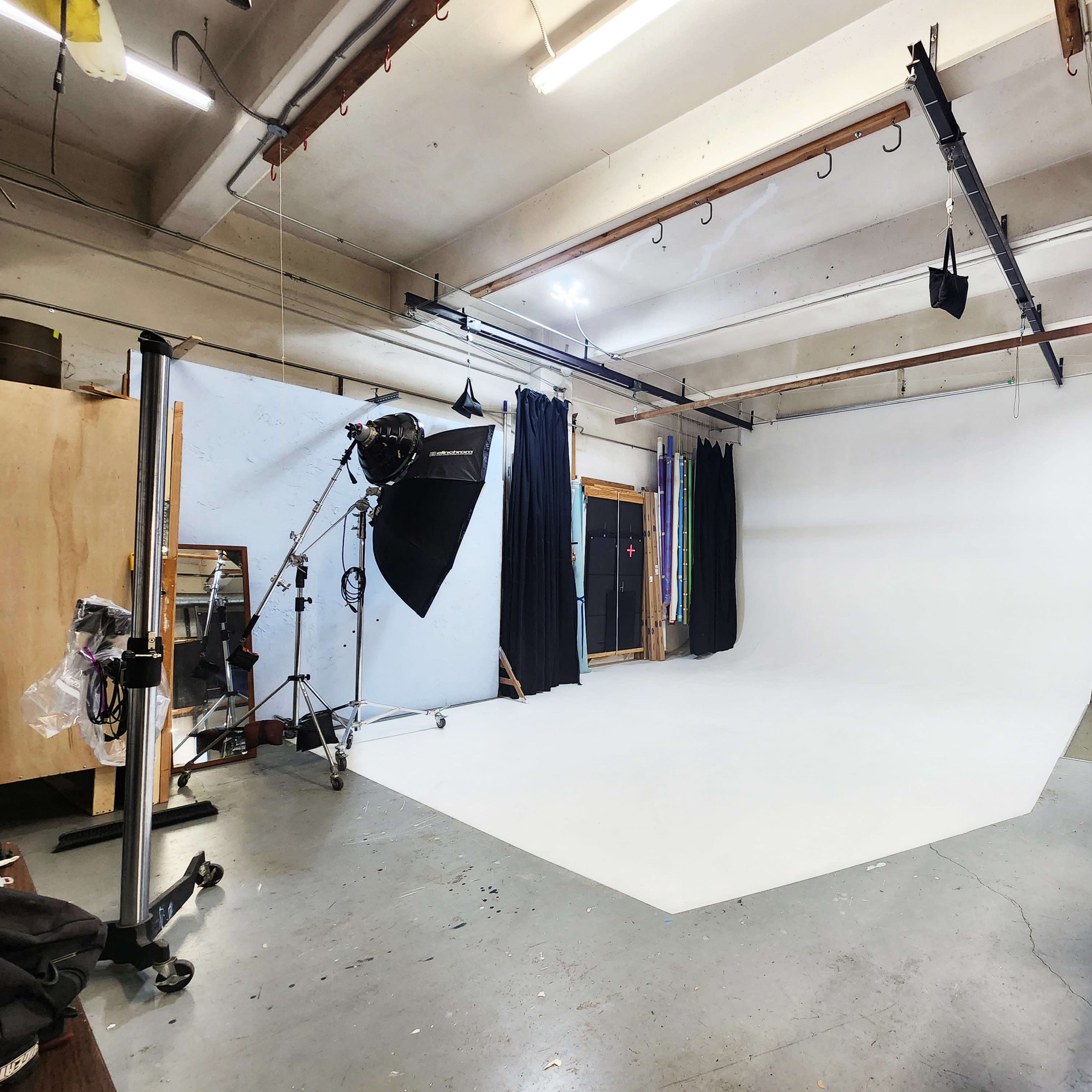 A photography studio with a large white backdrop, studio lighting equipment, and various props arranged around the space.