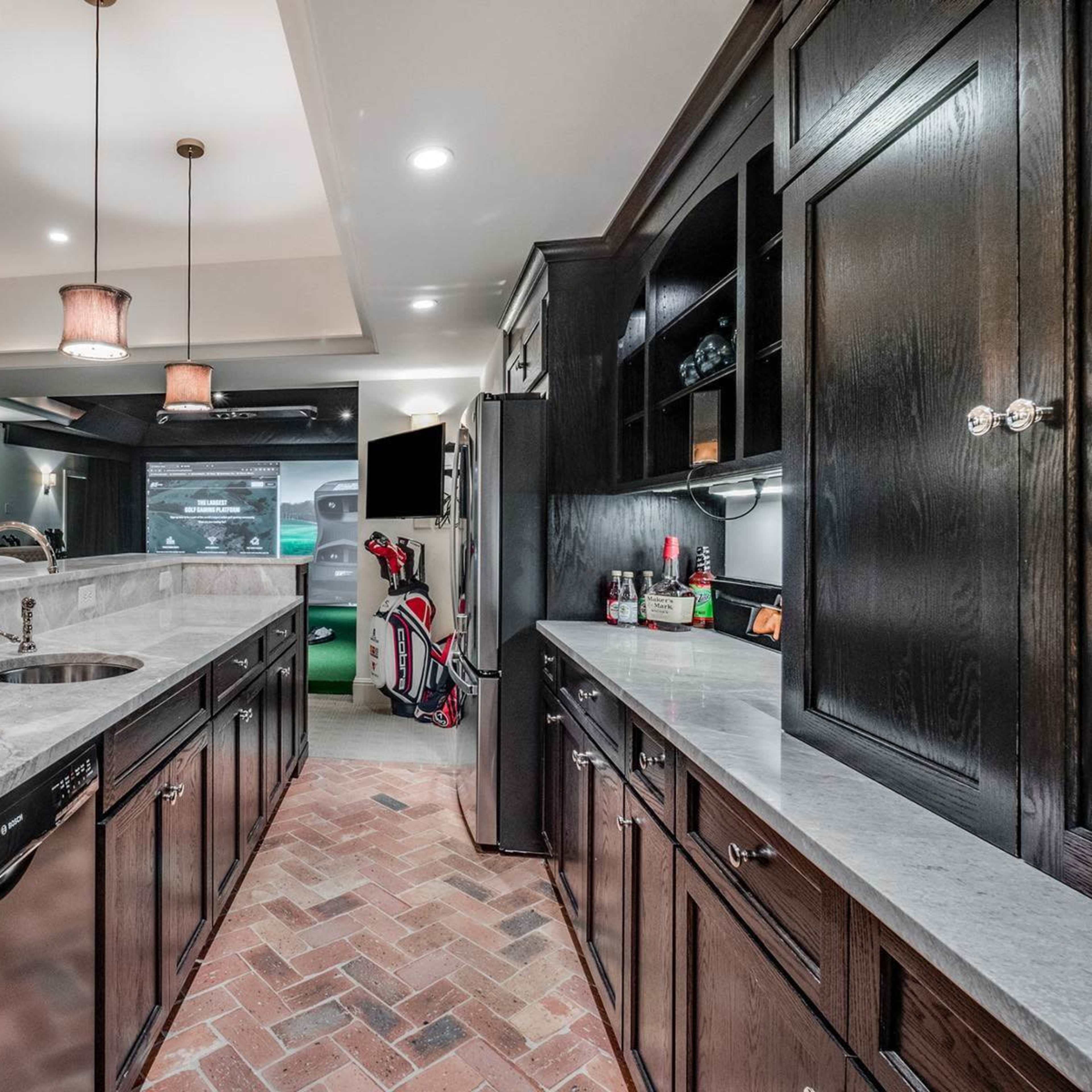 A modern kitchen with dark wooden cabinets, marble countertops, and brick flooring, featuring a sink and kitchen appliances in the background.