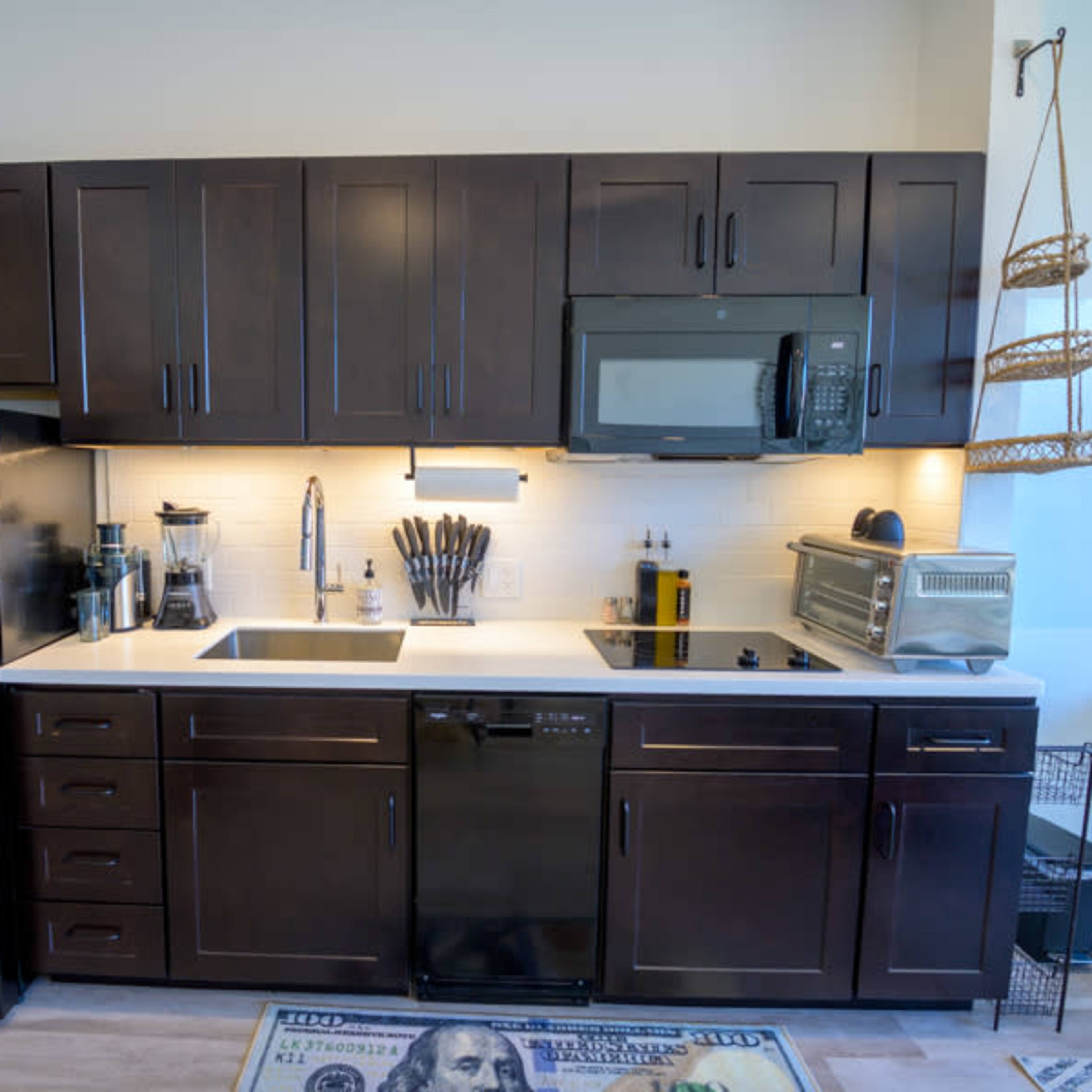 A modern kitchen equipped with dark wooden cabinets, a black refrigerator, a microwave, an oven, and a sink with kitchen utensils on the counter.