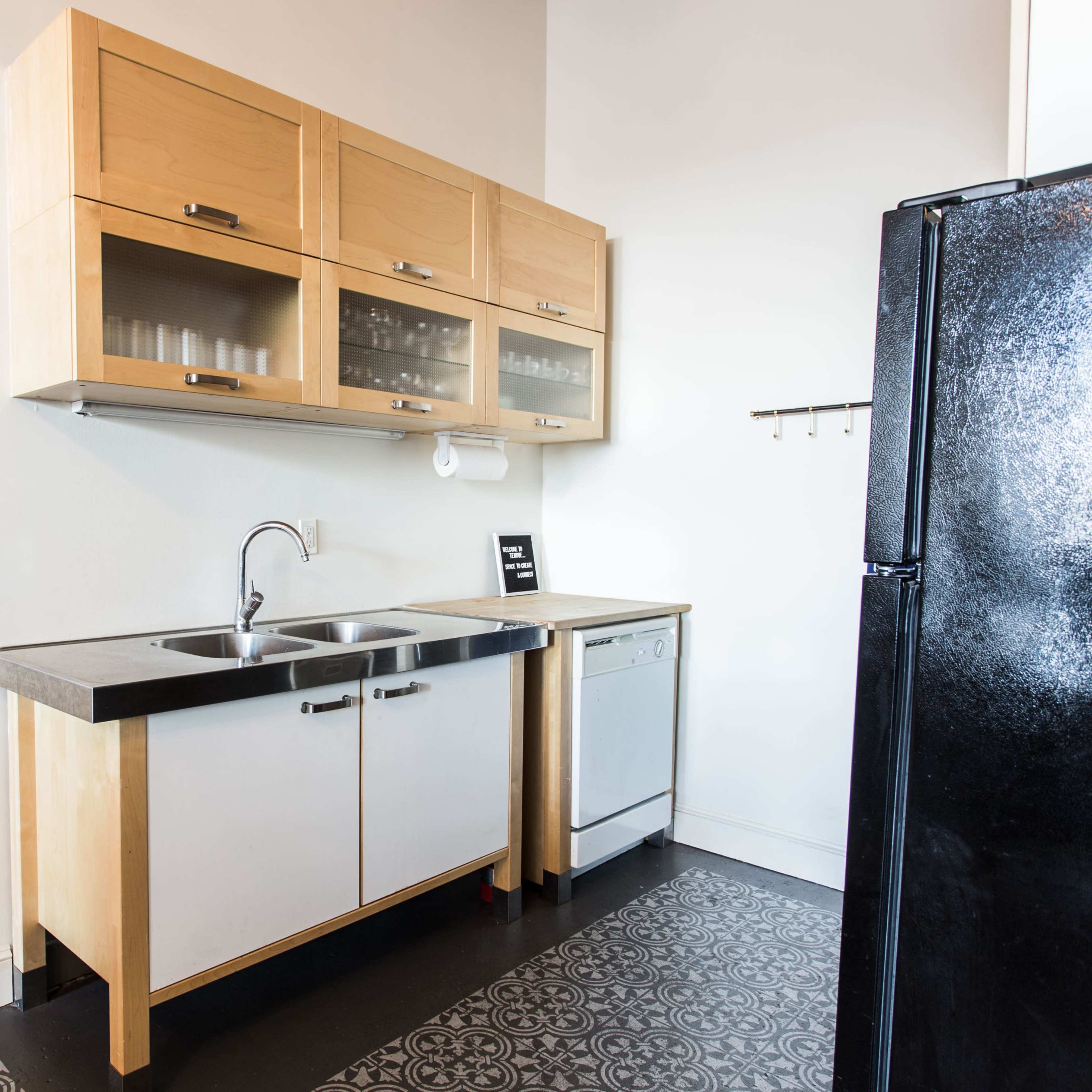 A modern kitchen with wooden cabinets above a double sink and a dishwasher beside a black refrigerator.