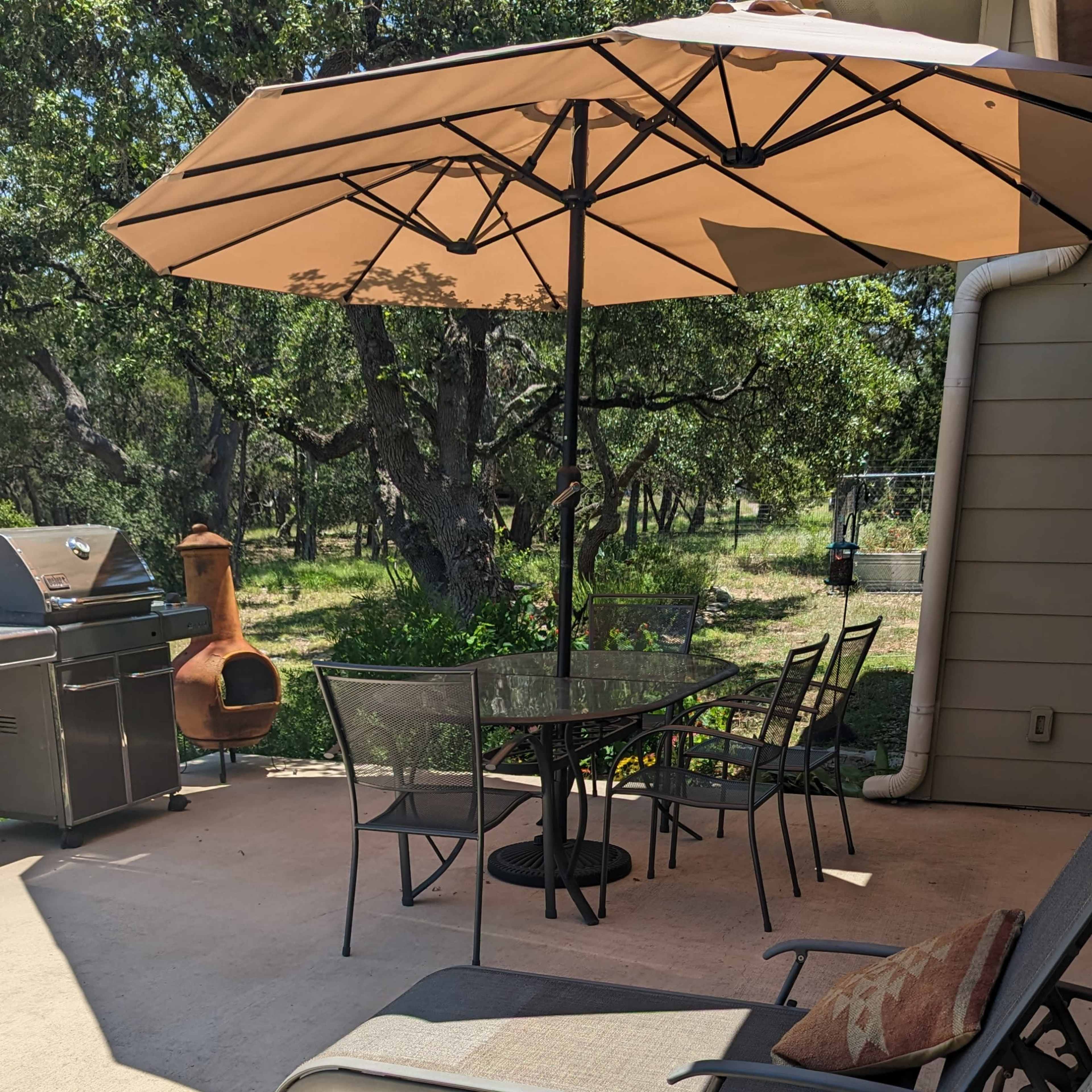 A patio area with lounge chairs, a table set under an umbrella, a grill, and a chiminea in a landscaped outdoor setting.